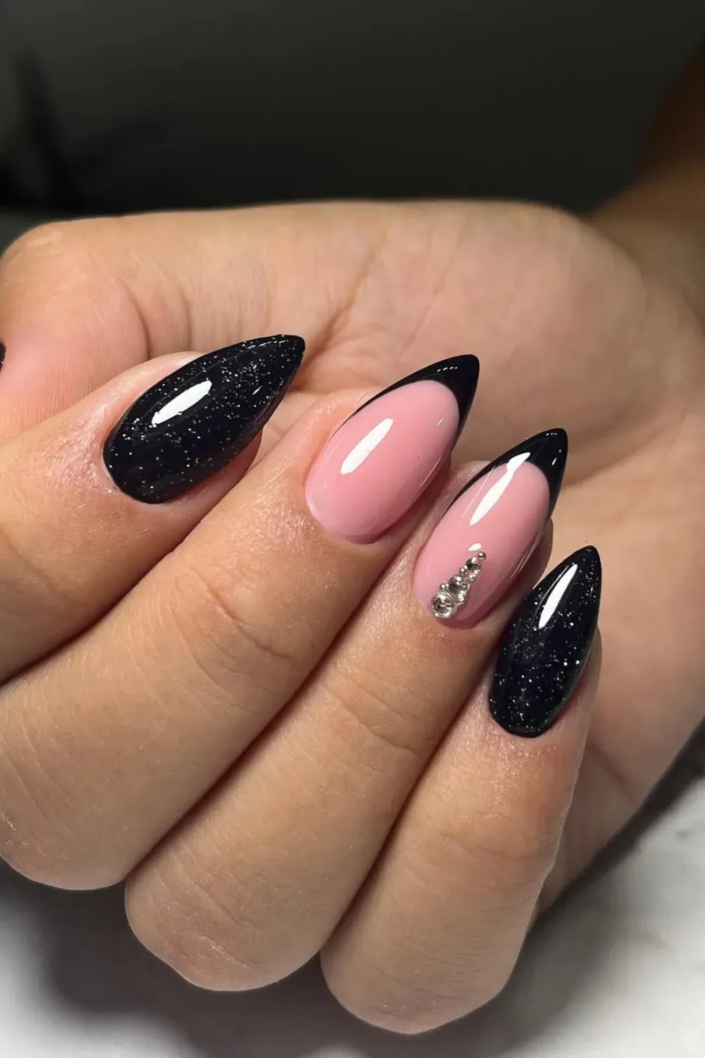 A modern black and pink nail design with a crystal accent on one nail, featuring glossy black tips and soft pink base