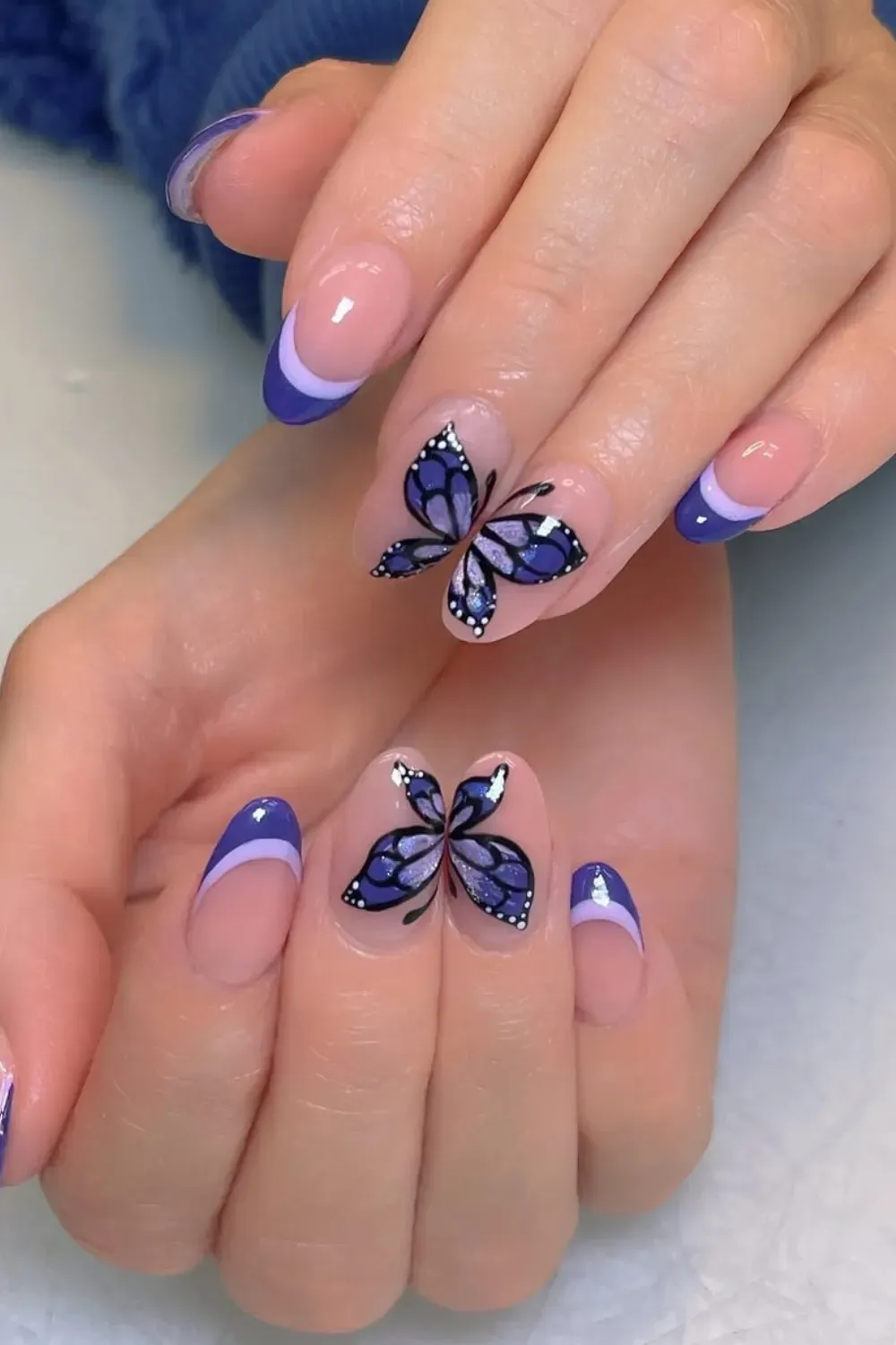 Butterfly design on nails with purple and blue French tips.