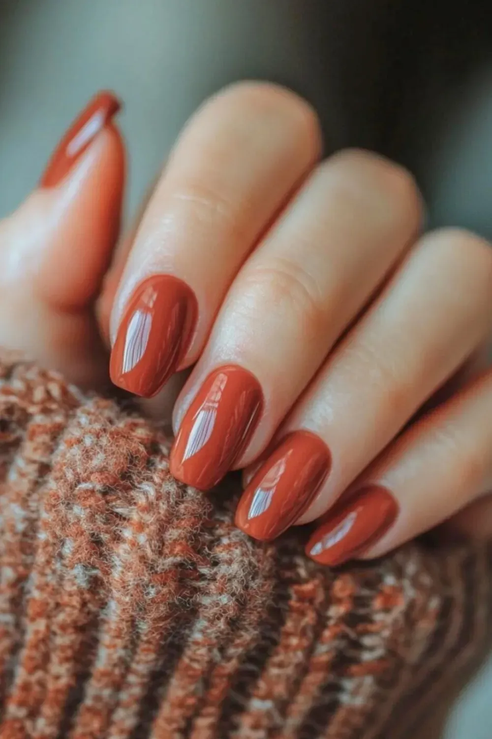 Terracotta-colored nails with a glossy finish, complemented by a cozy knit sweater, perfect for the fall season.