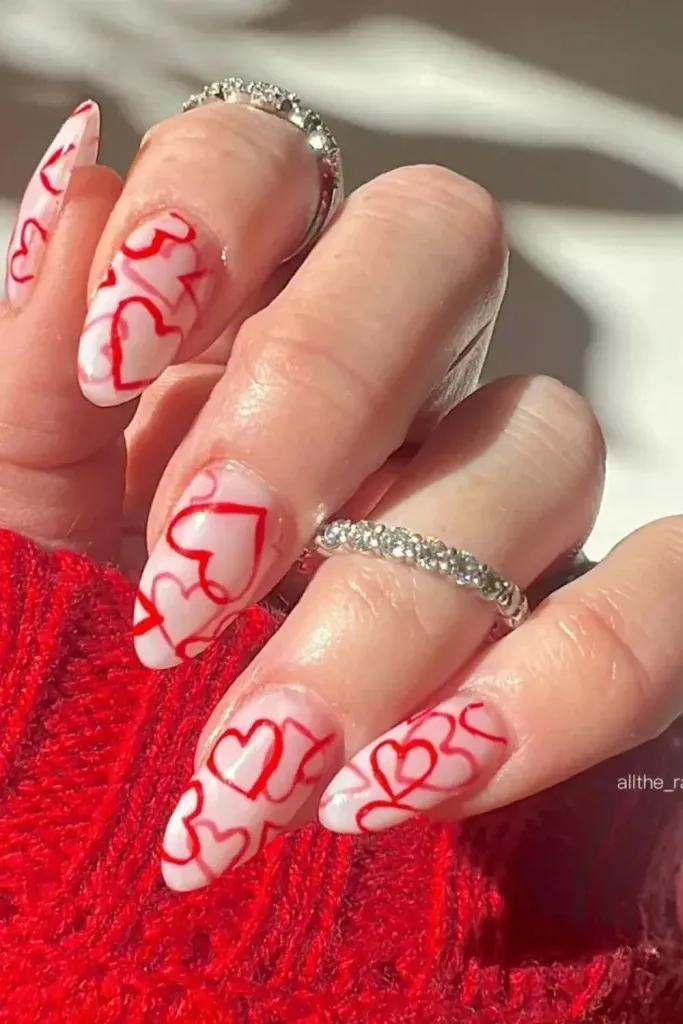 pointed nails painted in a light pink color with red heart outlines scattered across the nails.