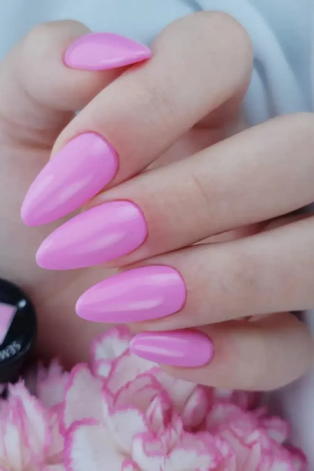 almond-shaped nails painted in a soft pink glossy finish. The nails are paired with a pink flower in the background