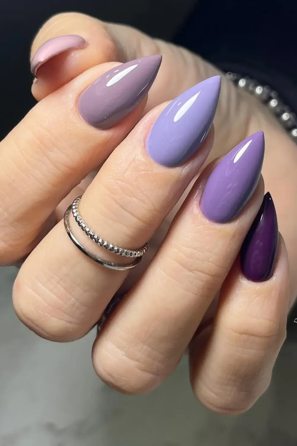 Trendy stiletto nails in various purple tones featuring a glossy finish, perfect for a chic and modern look