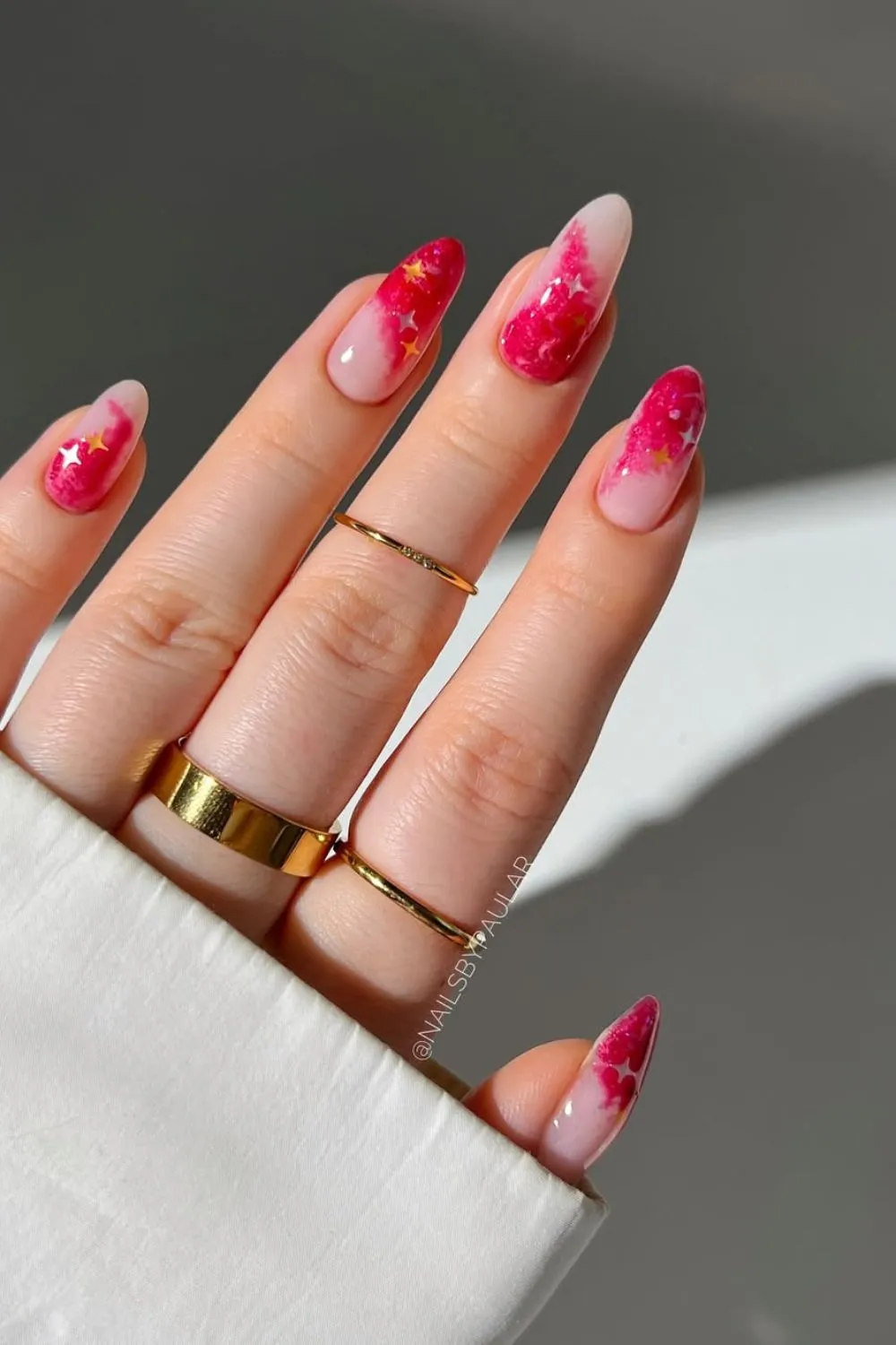 Red and Pink Galaxy Nails with Star Accents - Hand with almond-shaped nails featuring red and pink galaxy gradients with tiny stars