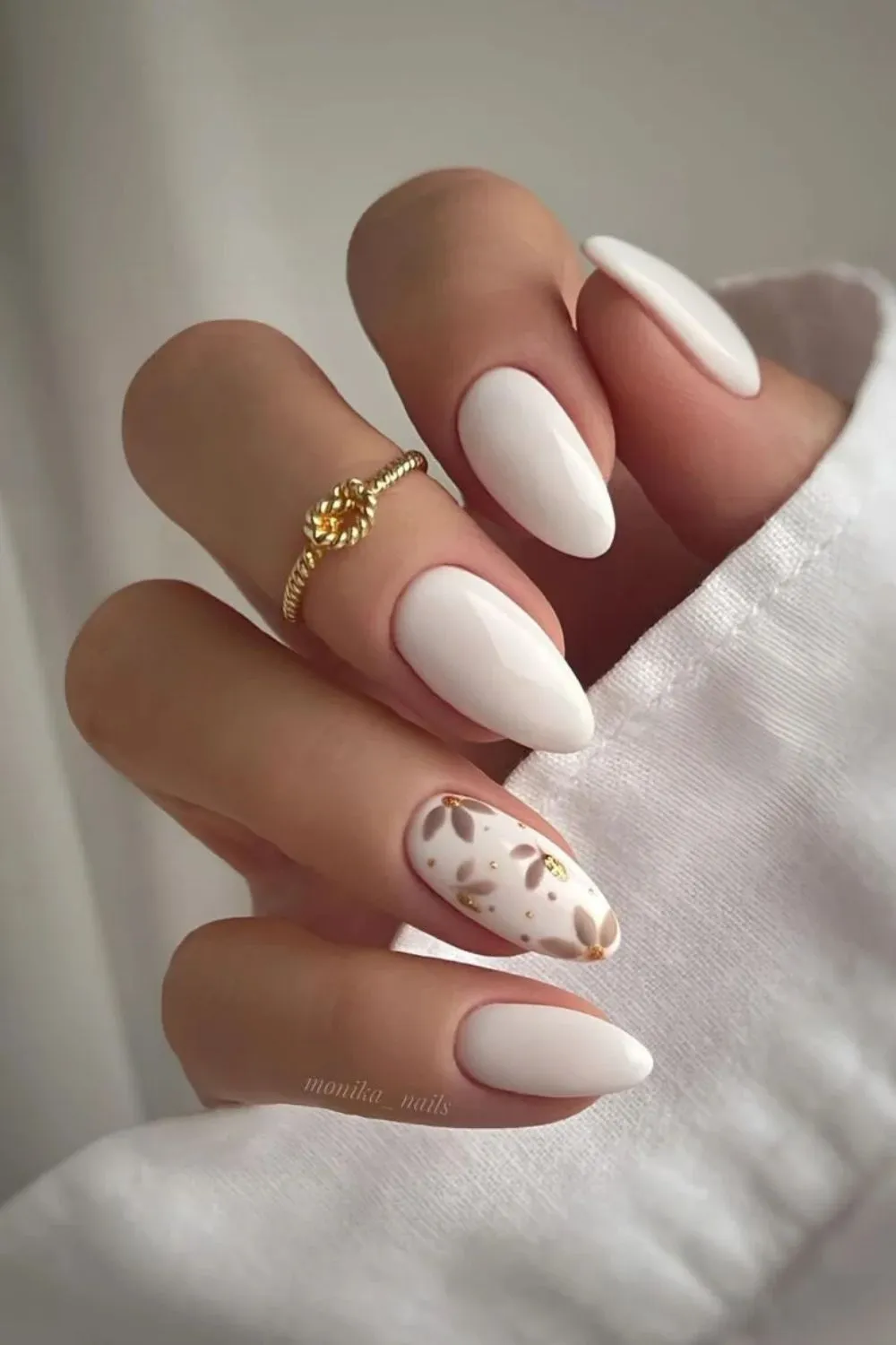 White Nails with Botanical Accent - White almond-shaped nails with one nail featuring beige and gold botanical design.