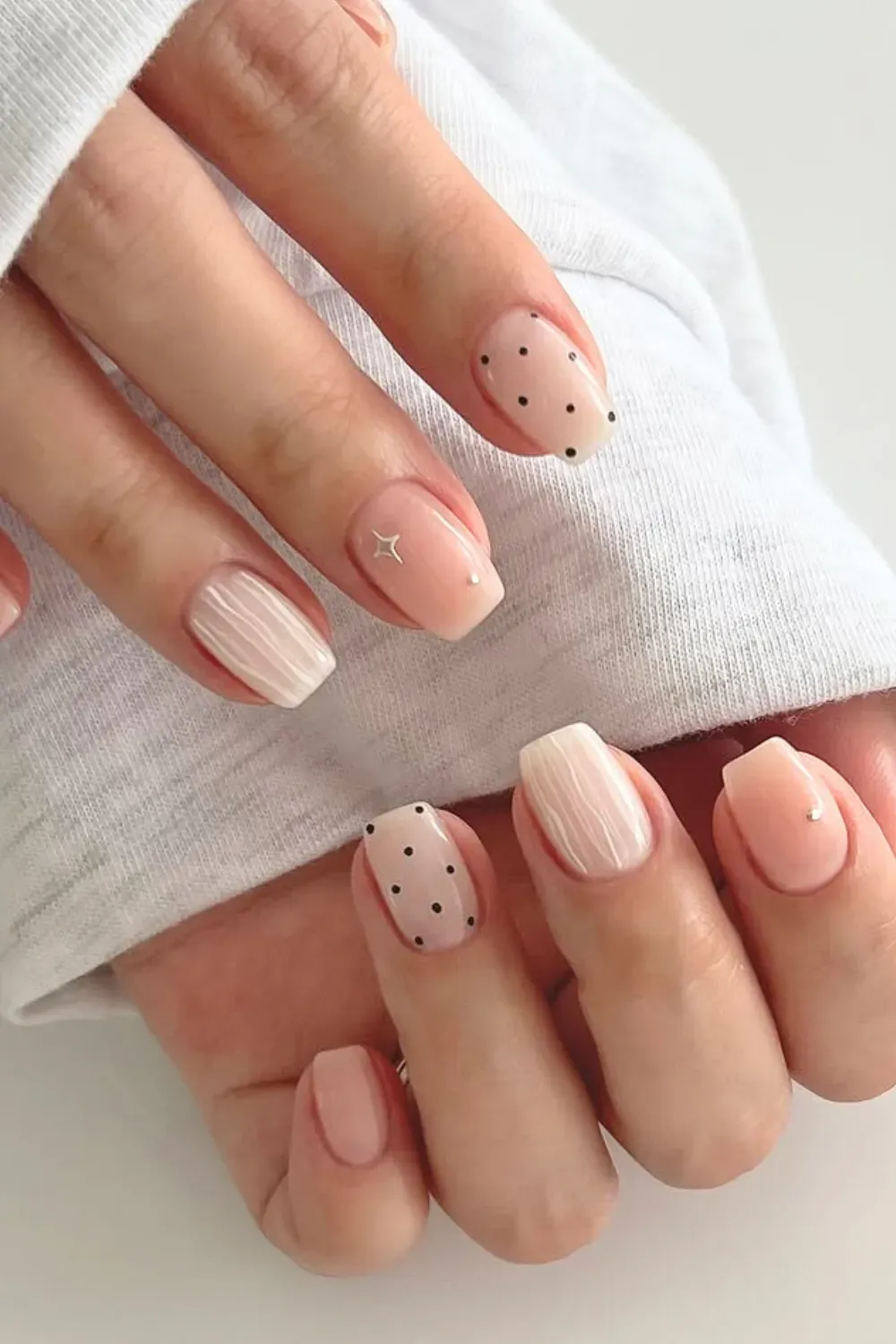 Nude nails adorned with small black dots arranged in a clean and minimalist design