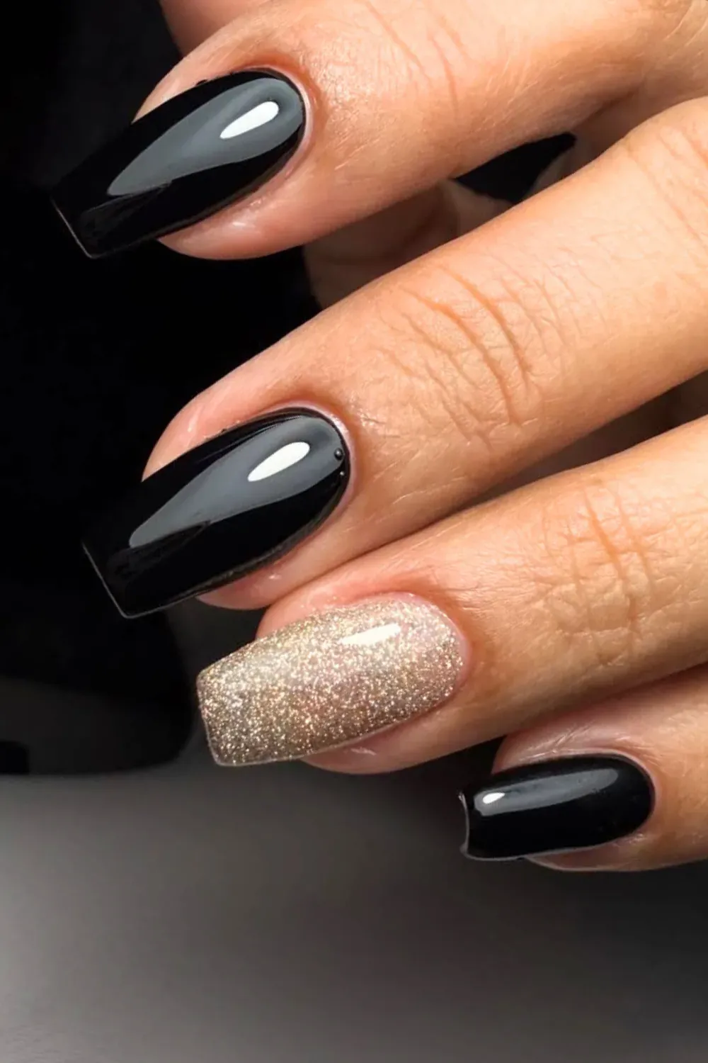 A hand with black and glittery gold nails for a striking, glamorous look.