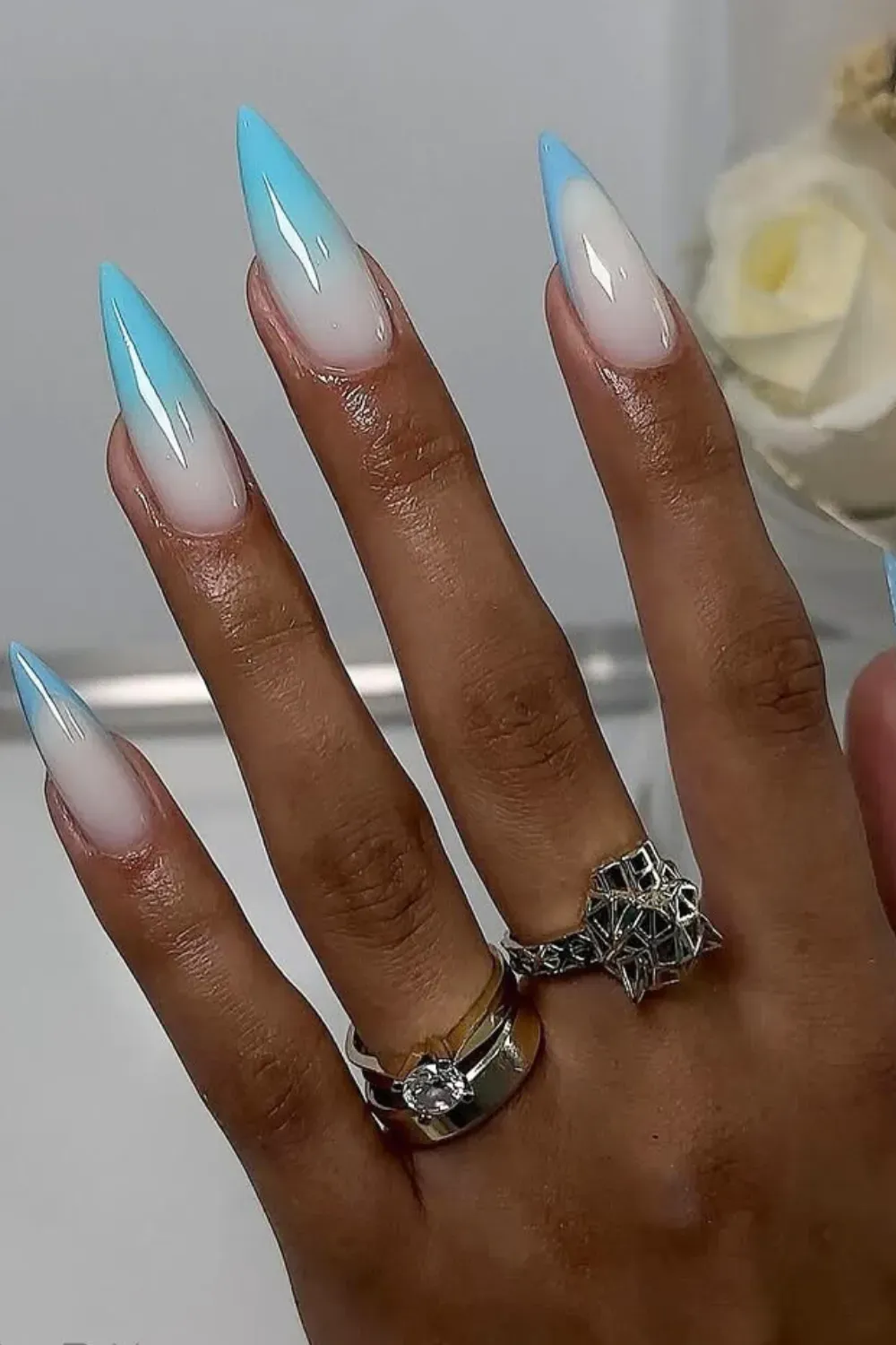 A hand featuring blue ombre pointed nails, complemented with rings
