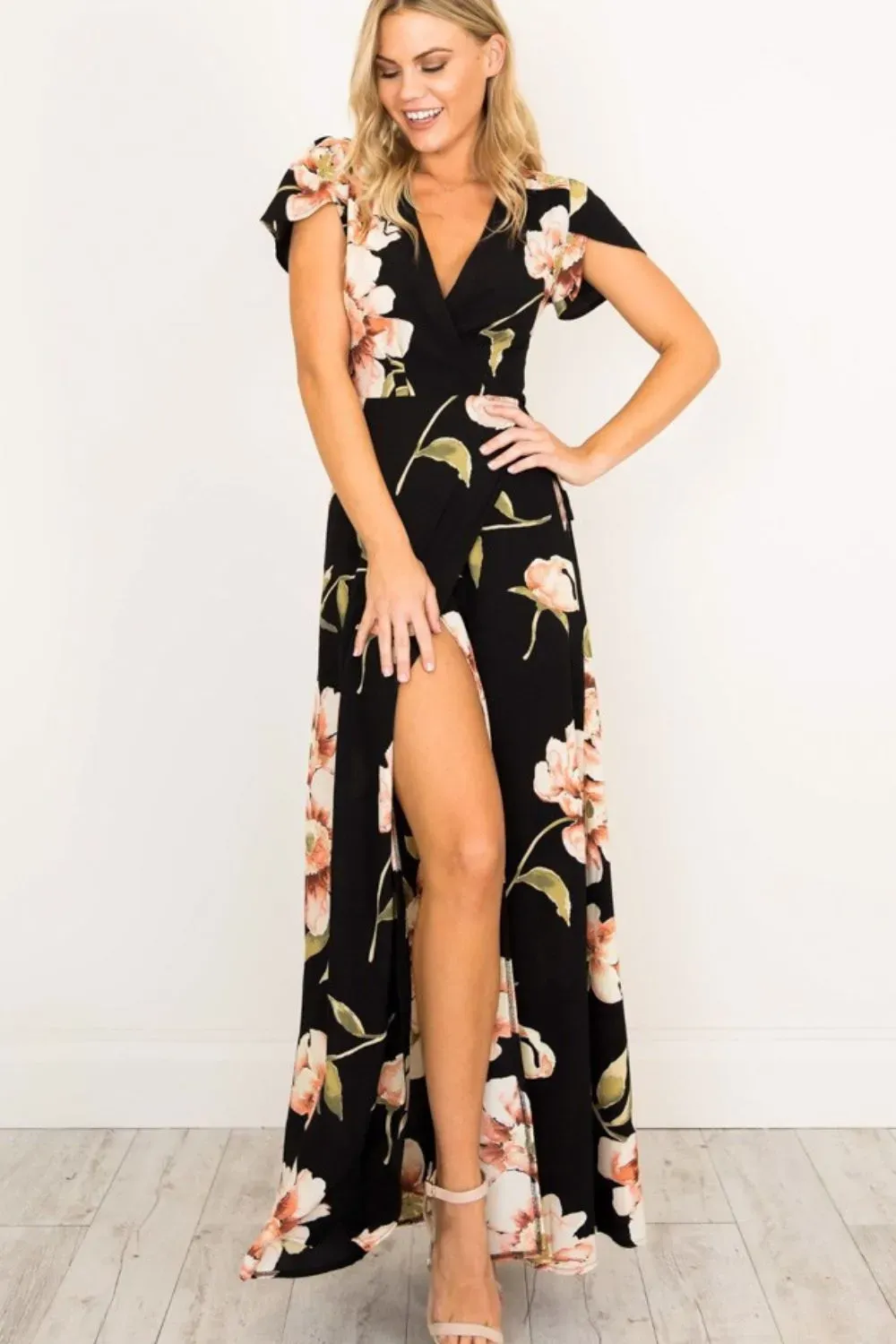 Woman wearing black floral wrap maxi dress with thigh slit and nude heels.