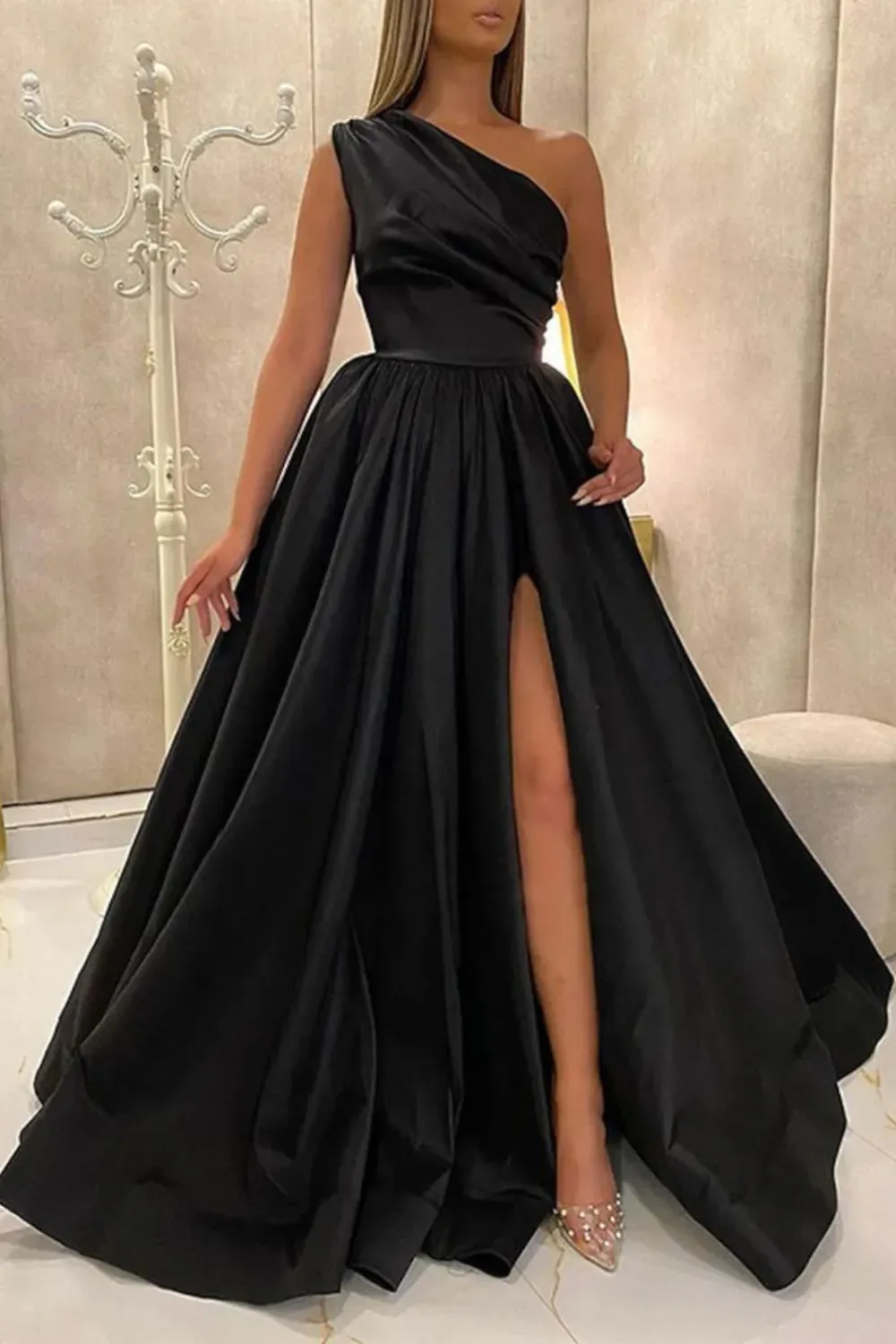 A sophisticated black one-shoulder dress with a voluminous, flowing skirt and a dramatic high slit.