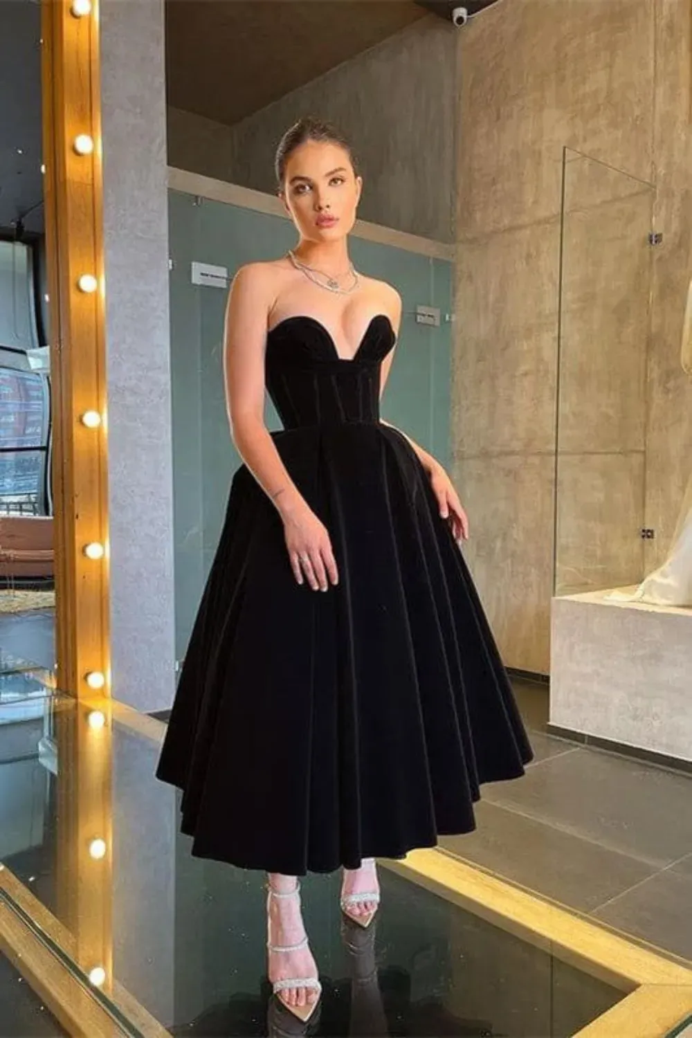 A model wearing a classic black dress with structured bodice and flowing skirt.