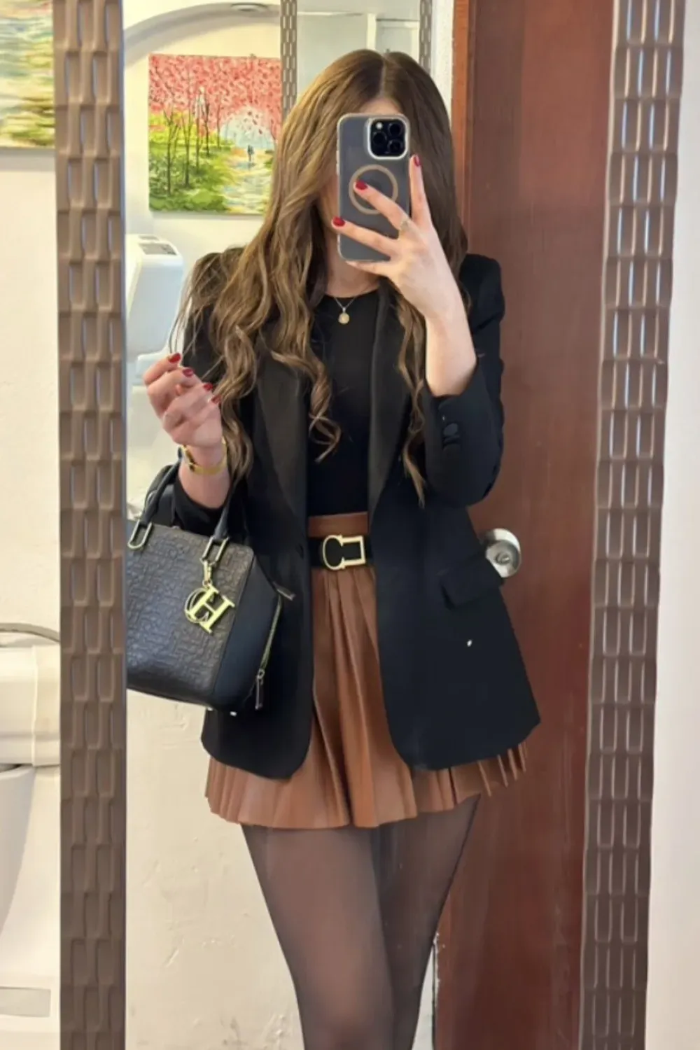 A woman in a leather top and flared skirt, wearing tights and boots, walking in an urban setting.