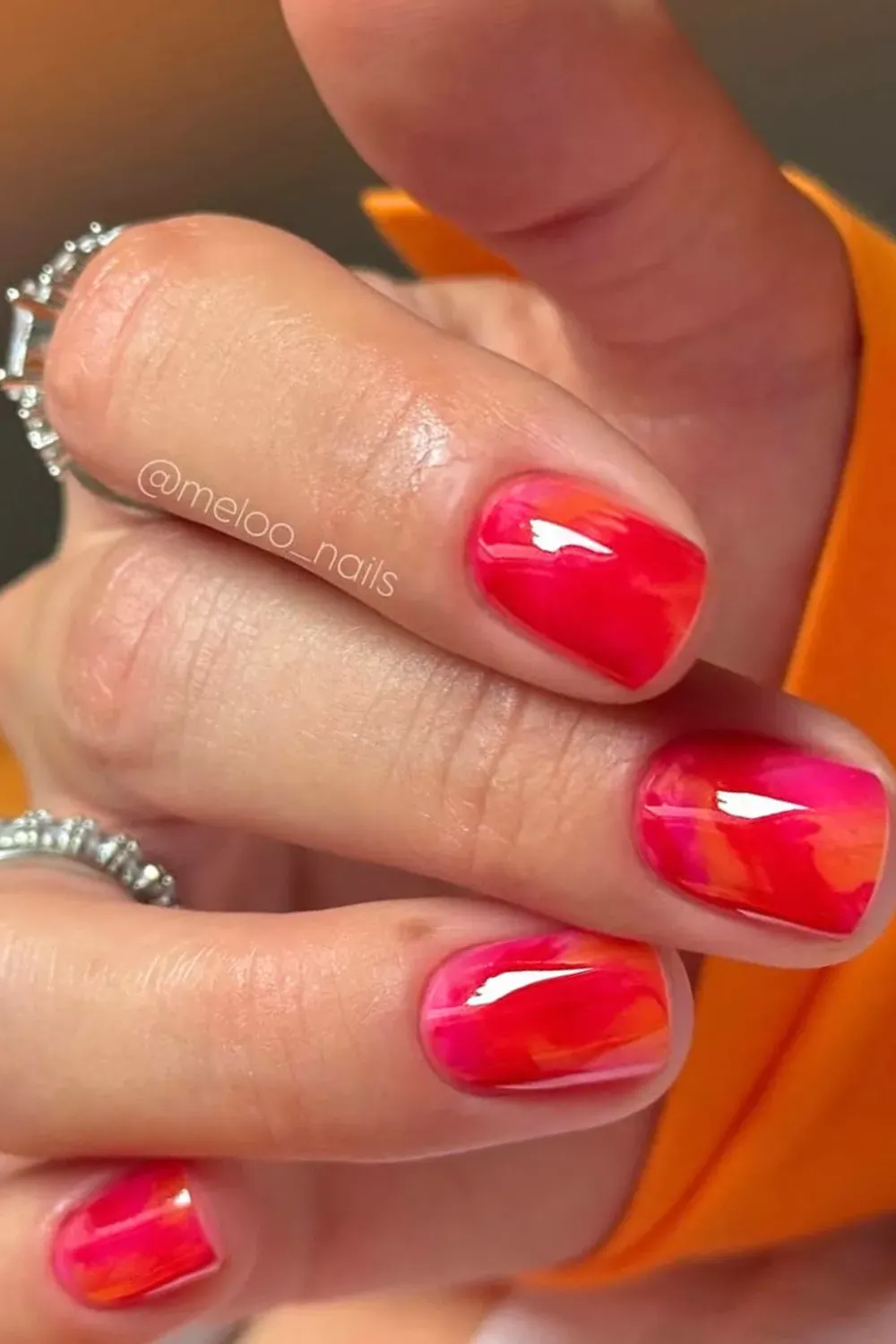 A close-up of nails featuring a stunning marble design in shades of pink, orange, and red, creating a bold and artistic look.