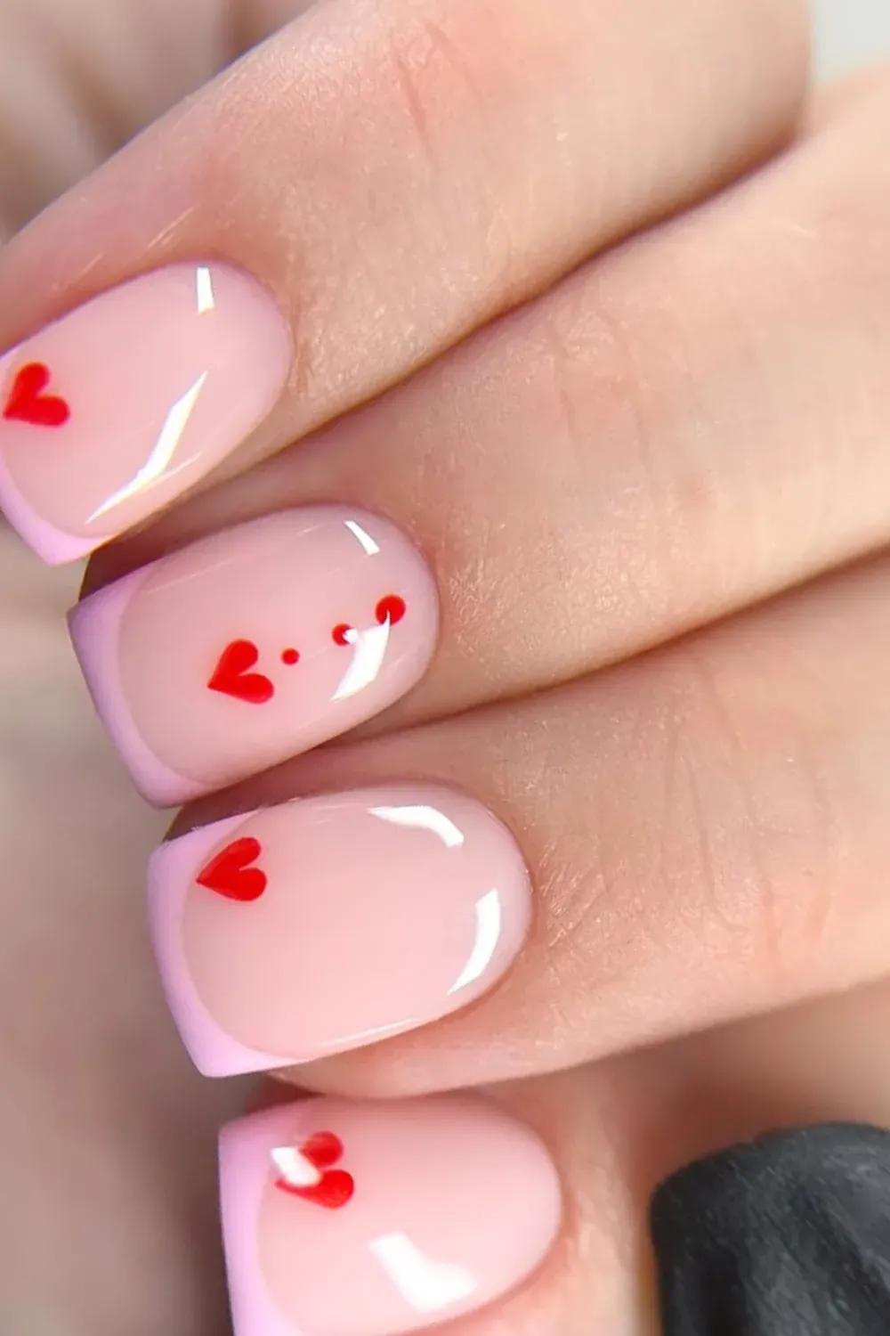 Nude nails with light pink French tips and red heart designs for a romantic vibe