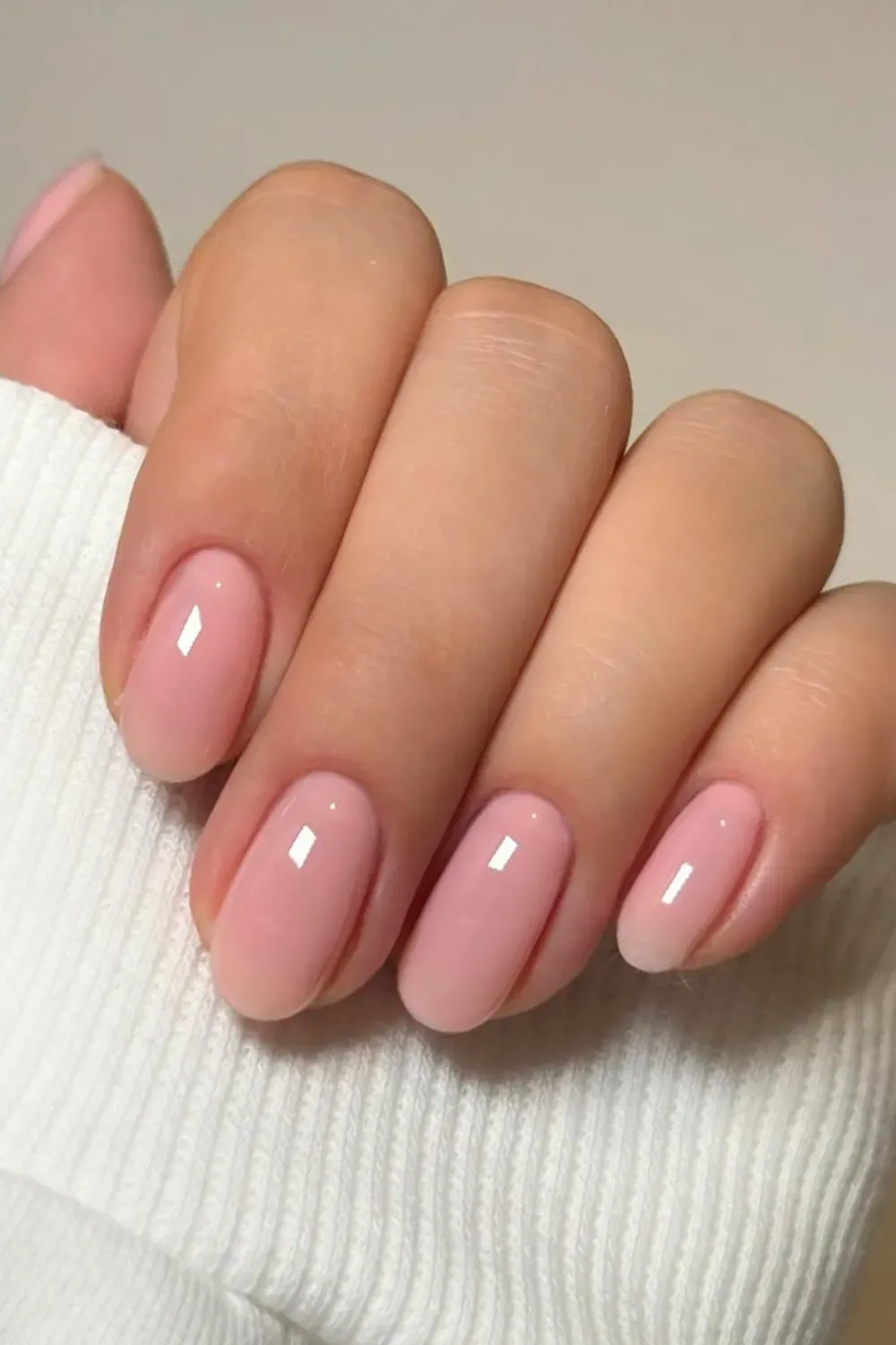 A close-up shot of elegant nude gel nails on a clean background with a soft white sweater