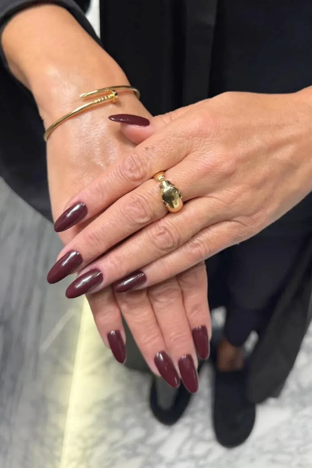 Elegant Burgundy Almond Nails with Gold Accessories - close-up of hands showcasing elegant chocolate brown almond-shaped nails, paired with a gold ring and bracelet