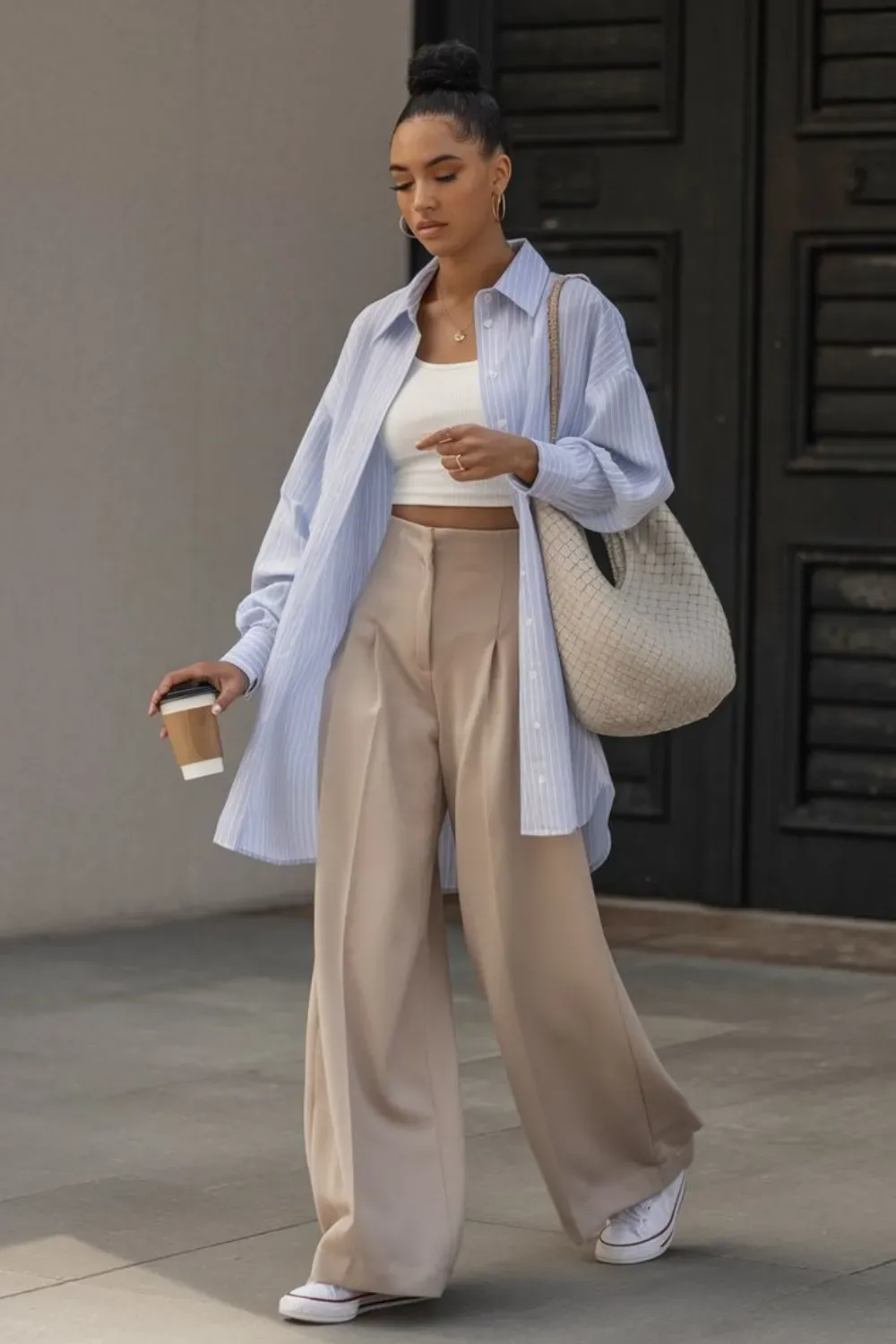 A woman in an oversized shirt and wide-leg pants walking with a coffee in hand