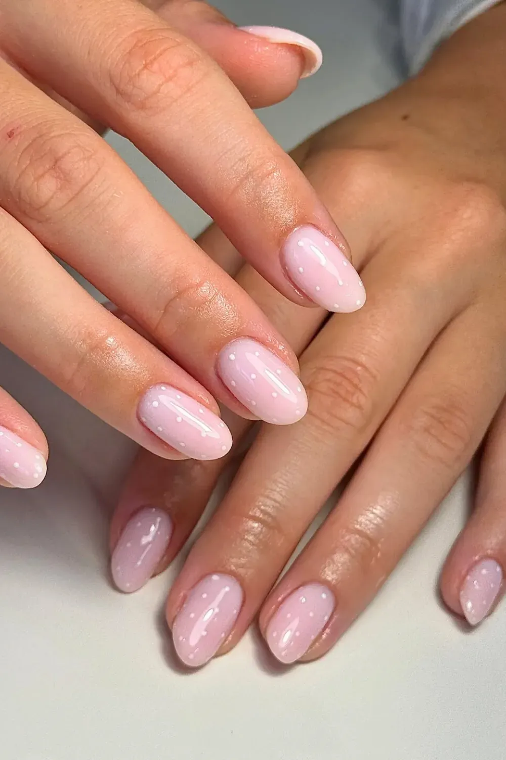 Soft pink ombre nails with white polka dots for a sweet and simple design