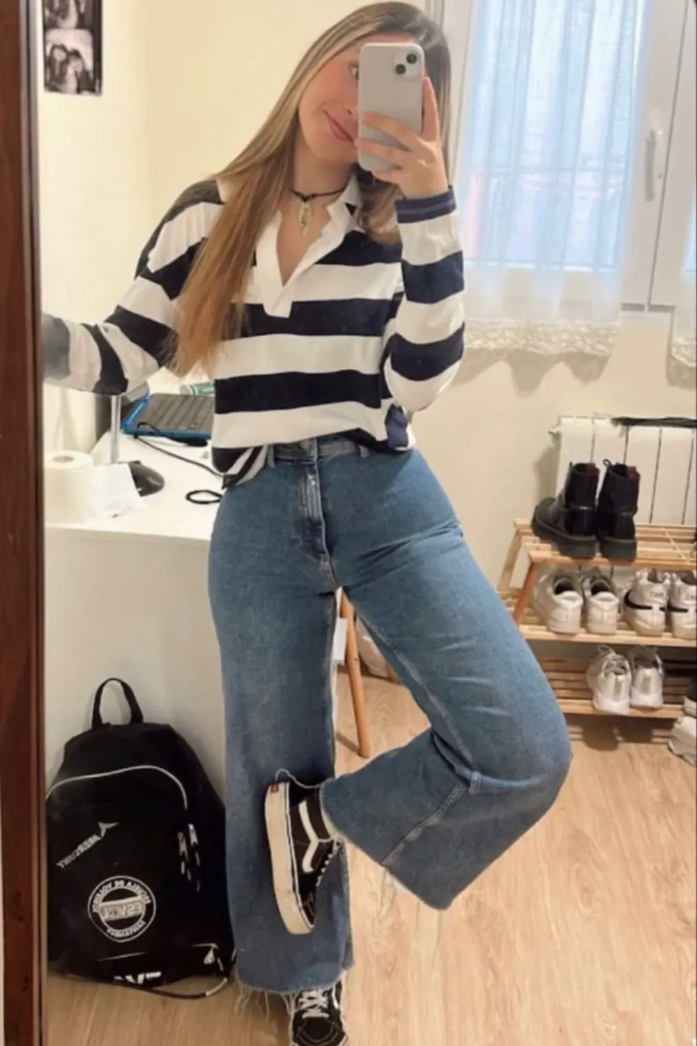 A woman wearing a casual T-shirt and baggy jeans, holding a phone in front of a mirror