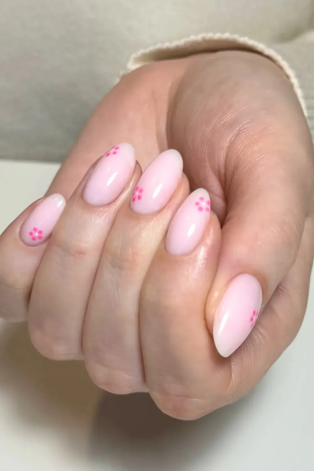 A close-up of soft pink nails adorned with small pink flowers on the tips, creating a chic and feminine look