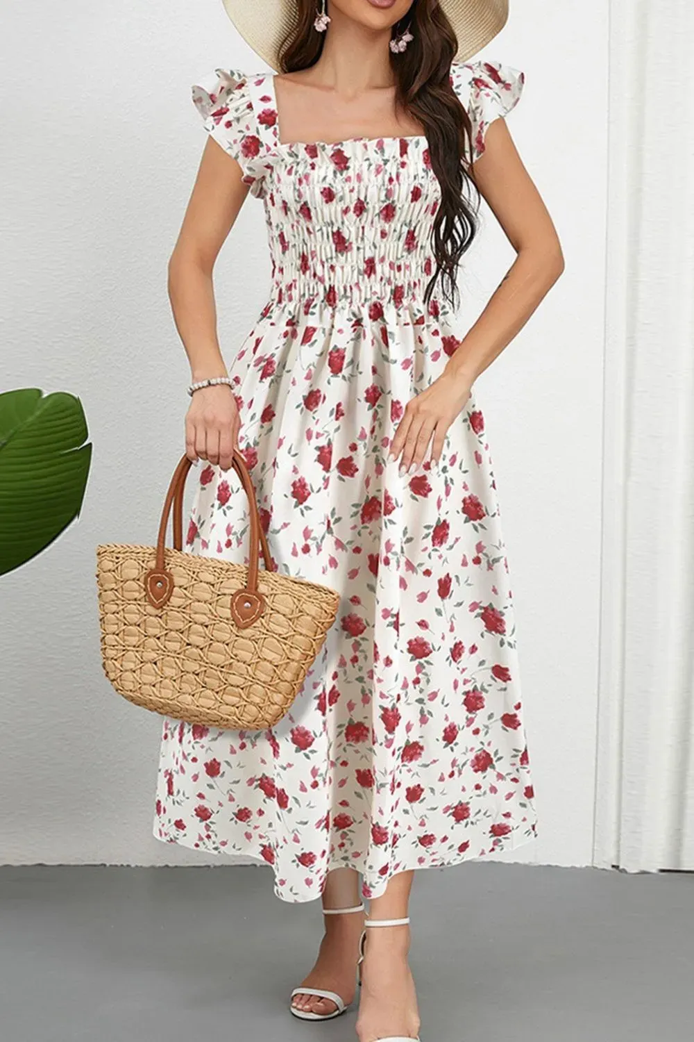 Woman in rose floral smocked dress holding a straw tote bag.