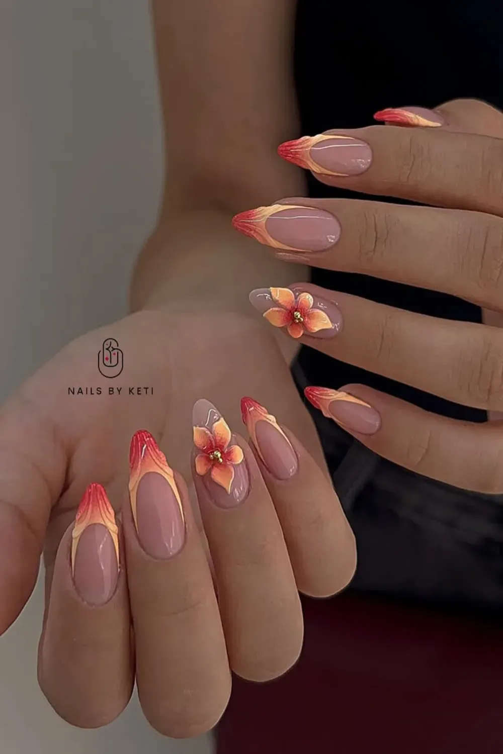 Bold tropical flame nails in orange, red, and yellow with 3D floral accents