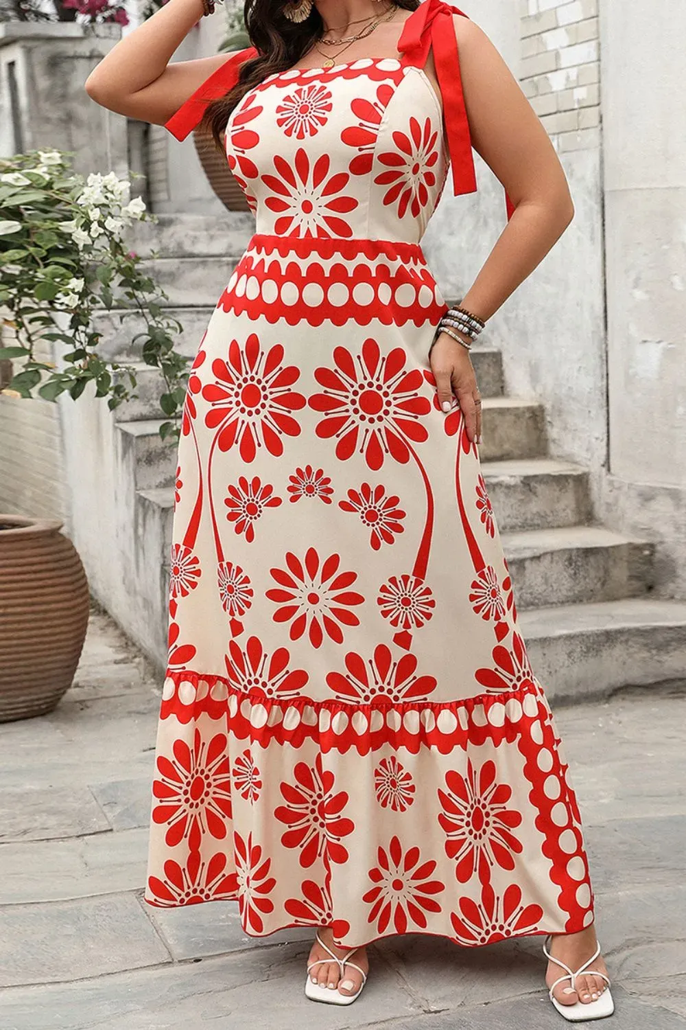 Woman in a red floral mini dress with shoulder ties, standing in soft sunlight.