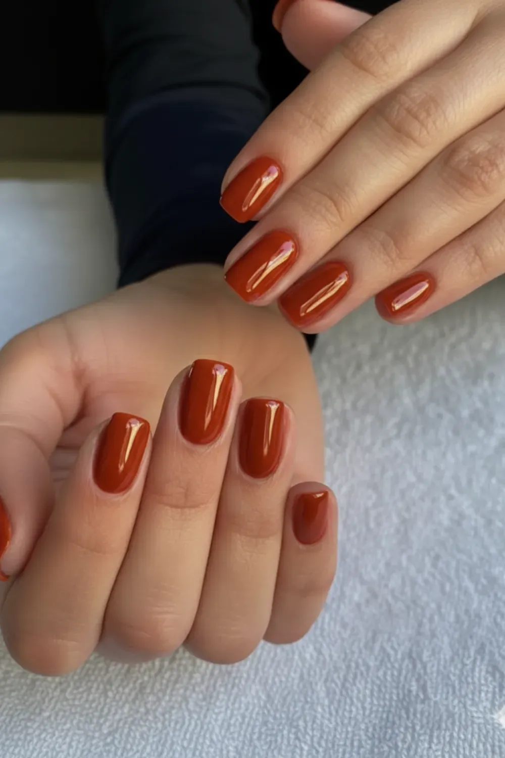 Glossy Burnt Orange and Rust Nail Art - A close-up of a hand with glossy, almond-shaped nails featuring a burnt orange and rust color palette with gold foil accents and black lines.