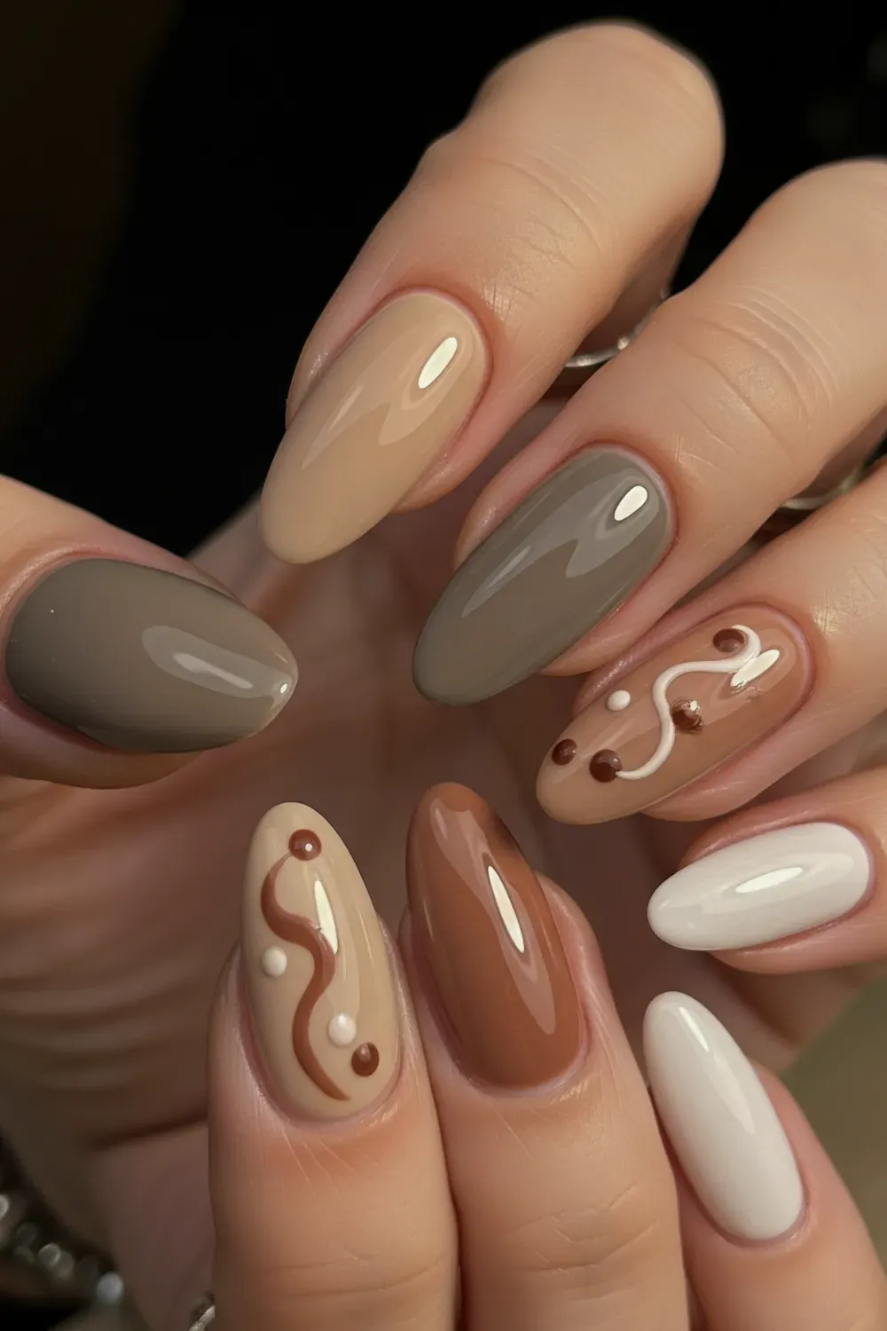  Earthy Neutrals Nail Art - A close-up of a hand with almond-shaped nails, each painted a different earthy neutral color like beige, taupe, and brown, with some nails having abstract designs