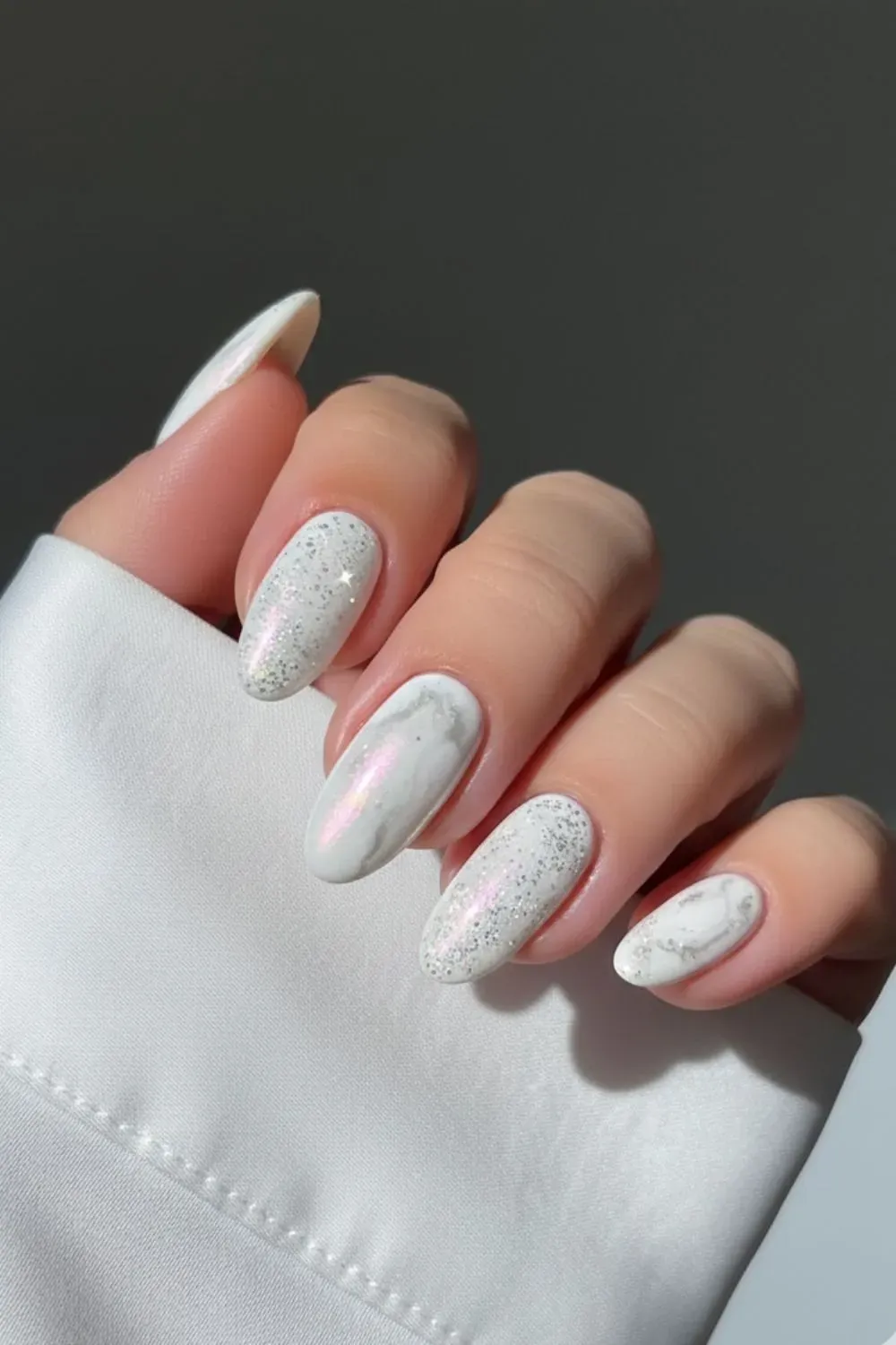 Milky white chrome nails with glitter and marble details.