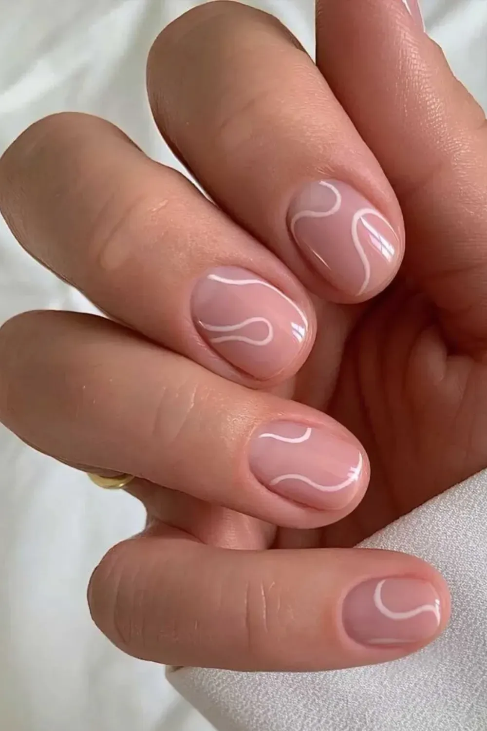 Short nude nails adorned with soft white swirls for a unique, contemporary design.