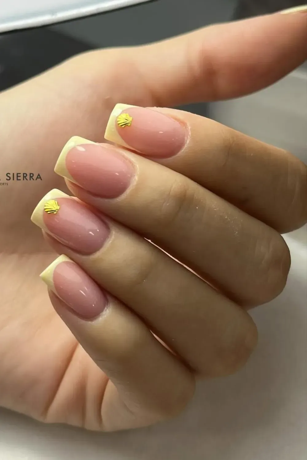 inimalist Yellow French Tips with Shell - Soft yellow French tips with a small gold shell accent on the nails