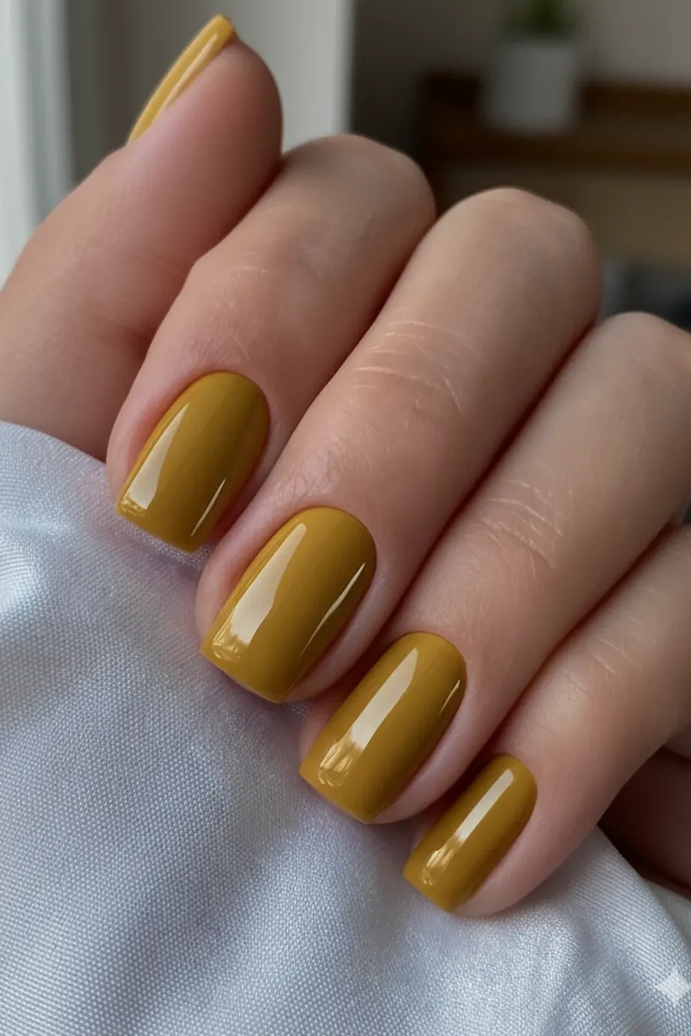 Glossy Mustard Yellow Nails - A close-up of a hand with glossy, short, squared nails painted in a solid mustard yellow color