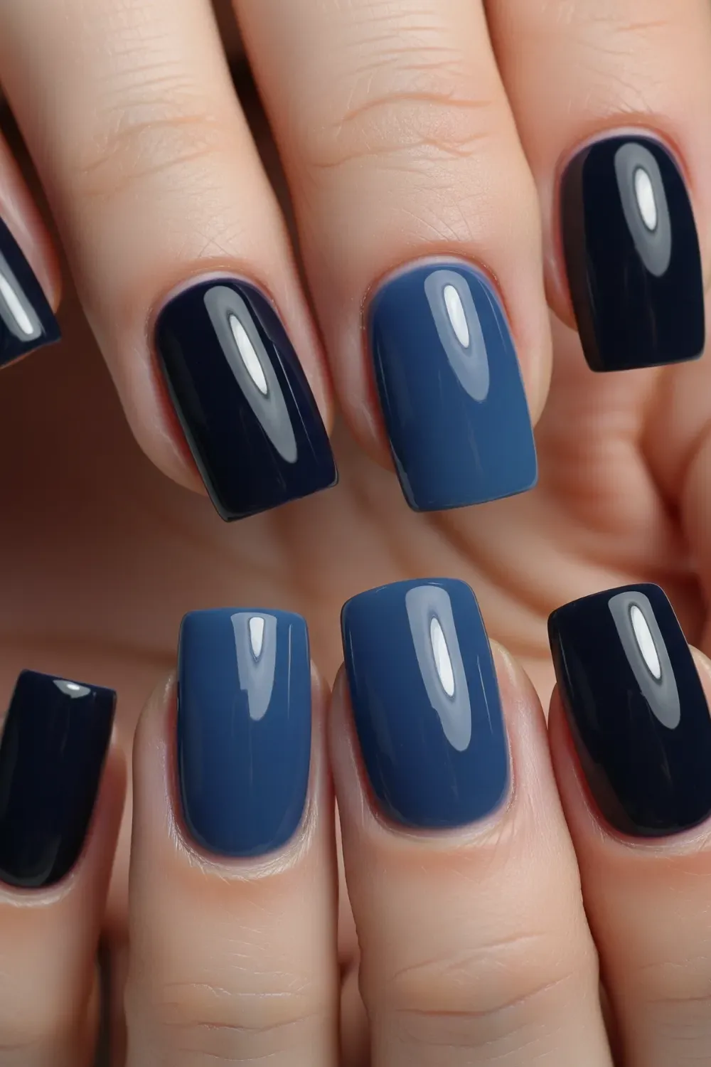  Glossy Navy Blue Gradient Nails - A close-up of a hand with short, squared nails painted in various shades of glossy navy blue, from dark to medium blue, creating a chic gradient effec