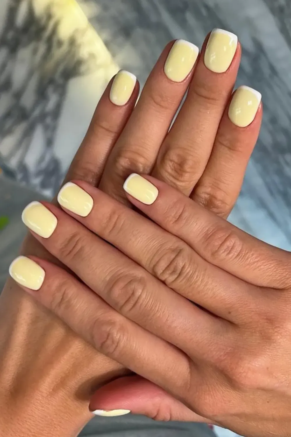 A minimalist French manicure featuring soft yellow tips with a clean, glossy finish, complemented by white French tips on a natural nail base