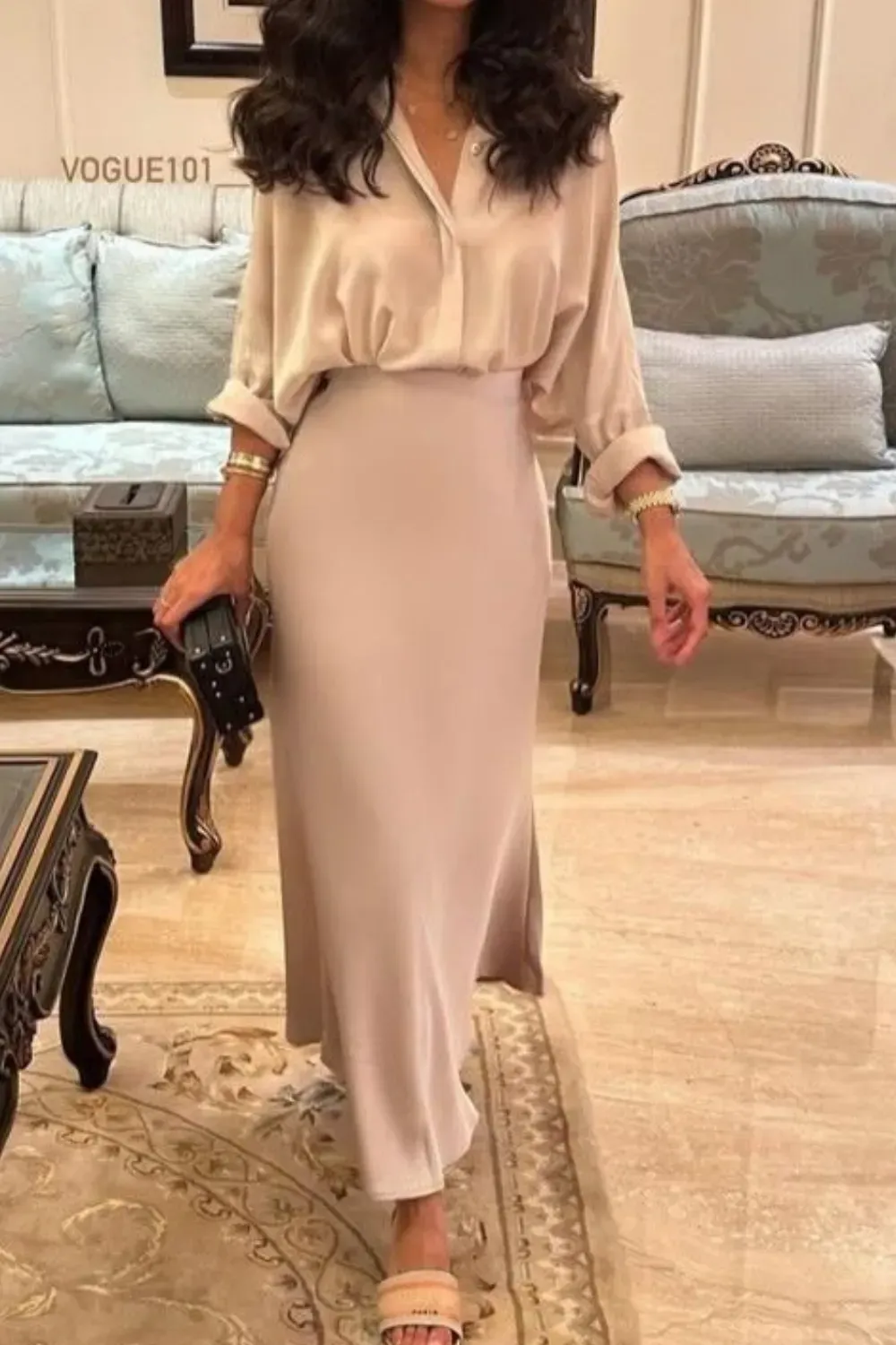 Flowy Silk Blouse and Nude Satin Midi Skirt	Woman in a luxurious living room setting wearing a loose, oversized nude silk button-down blouse and a high-waisted fitted satin maxi skirt in a matching beige tone.