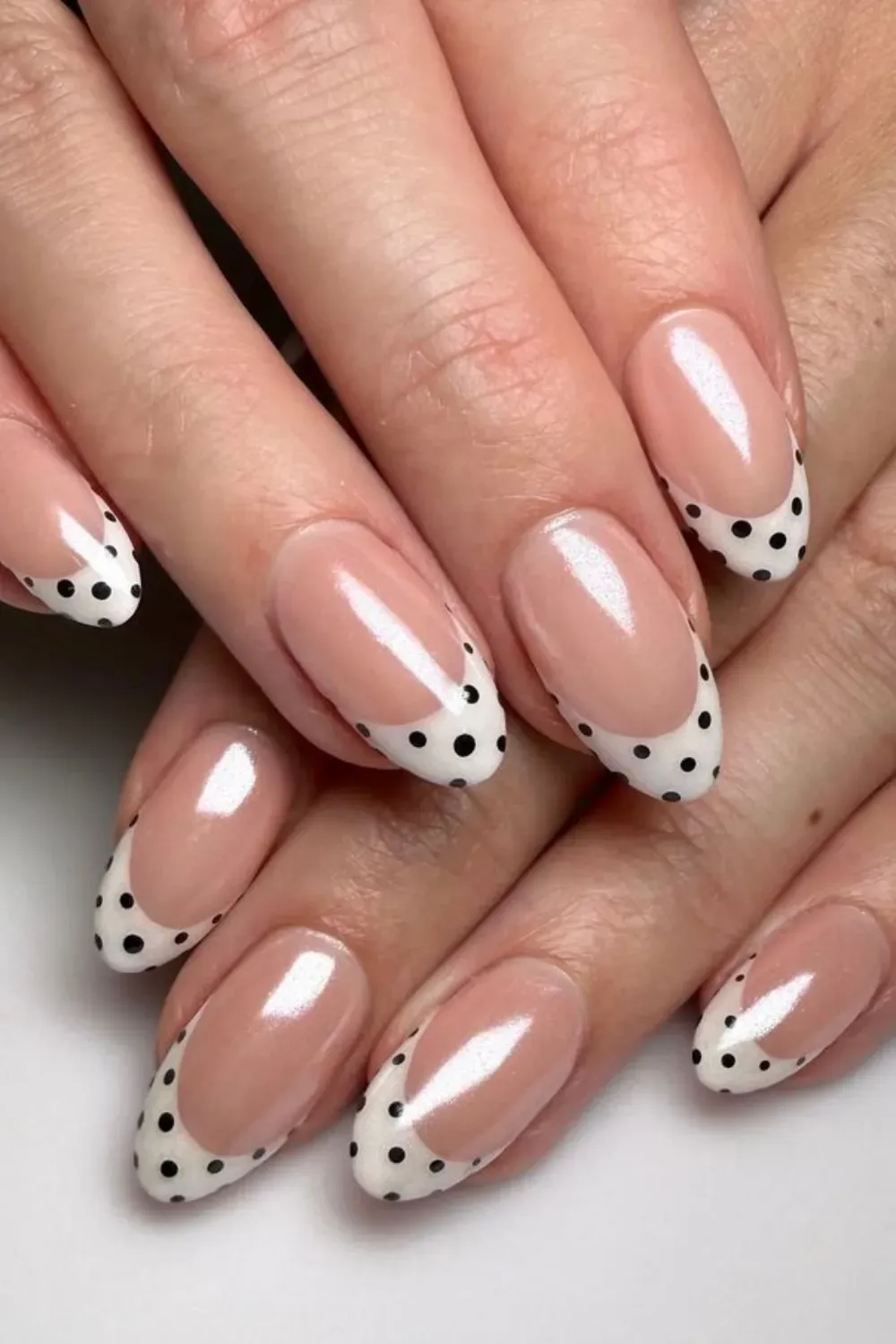 Natural-look nails with a shimmery nude base and white French tips accented with small black polka dots.