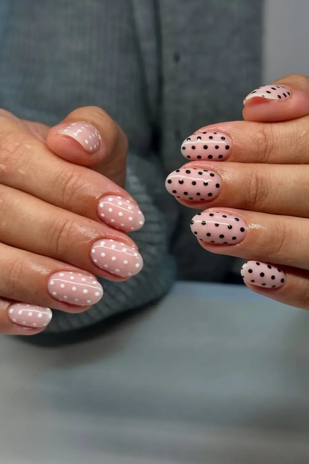 Short oval nails with a sheer pink base, alternating between white and black polka dot patterns on different fingers.
