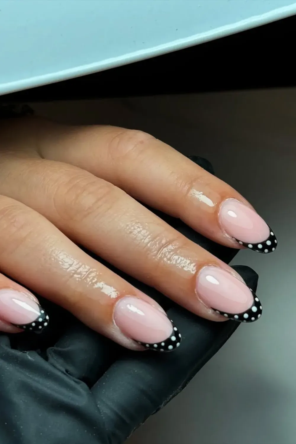 Almond-shaped nails with a clear nude base and classic black French tips accented with small white polka dots.