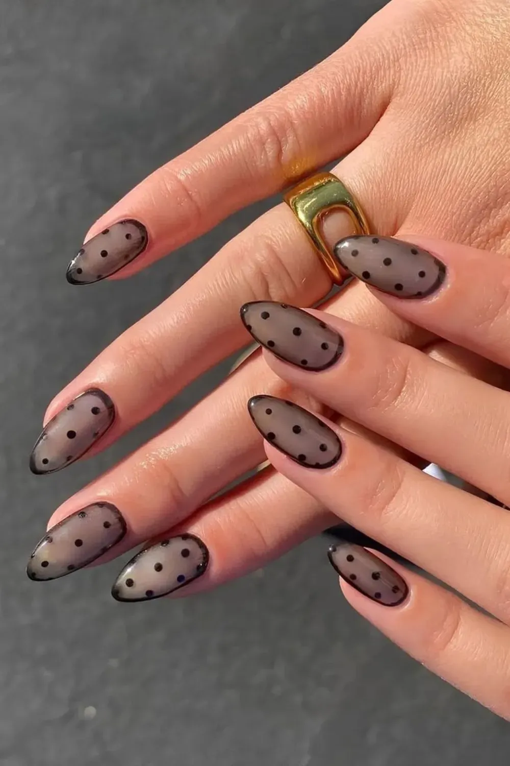 Almond nails with a sheer, smoky gray base and small black polka dots, mimicking the look of sheer dotted hosiery.