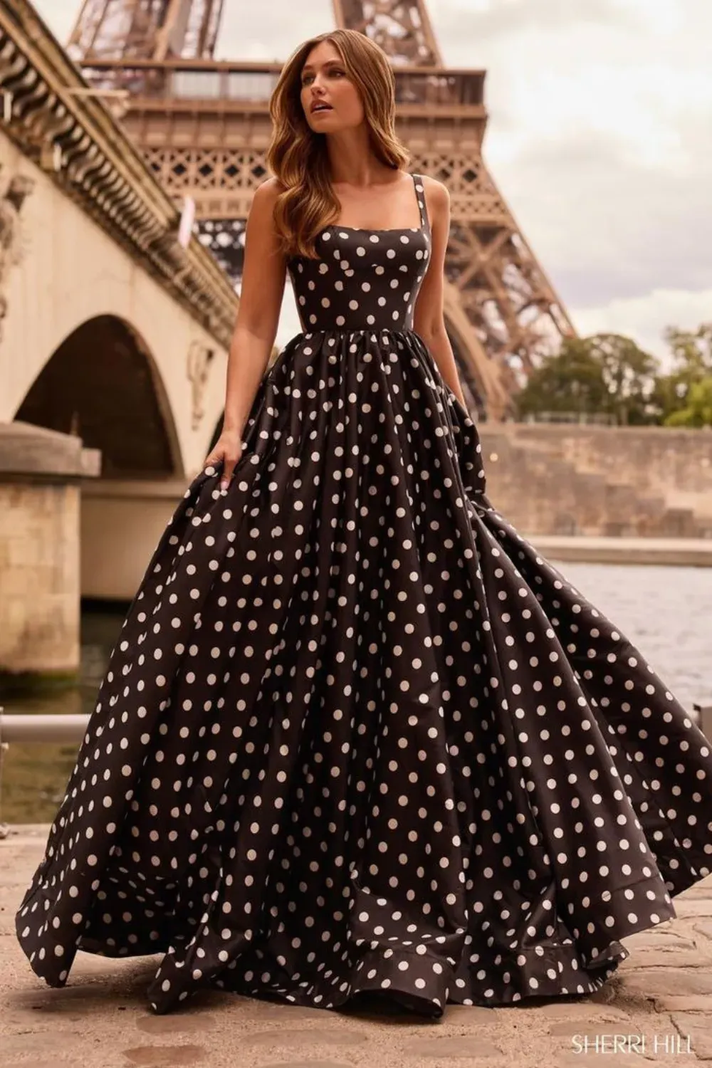 Black Polka Dot Ball Gown in Paris	Woman standing near the Eiffel Tower wearing a dramatic black and white polka dot ball gown with a full skirt and square neckline.