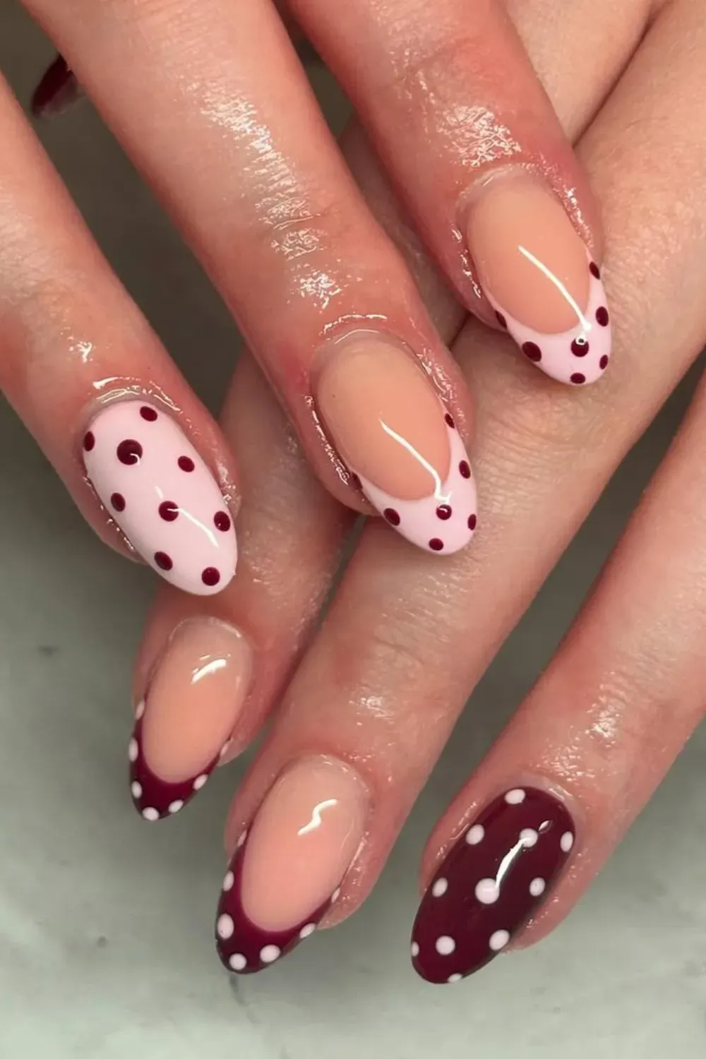 Oval nails with a mix of light pink and deep burgundy base, featuring contrasting polka dots and French tip designs.