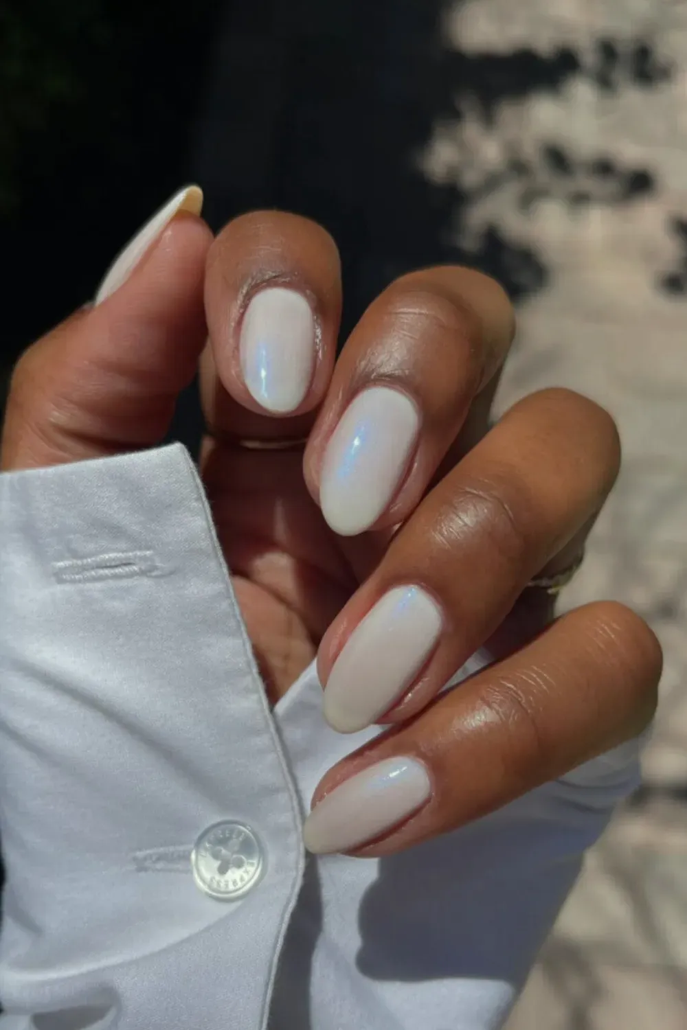 Iridescent Shimmery Milky White Nails for an Elegant Finish - Almond-shaped nails on a dark skin tone with a white milky base and a luminous, iridescent, pearlescent top coat.