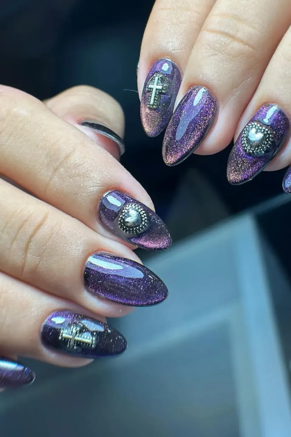 Purple Cat Eye Nails with 3D Charms	Almond-shaped nails in a deep purple magnetic polish adorned with silver 3D cross and heart charms.