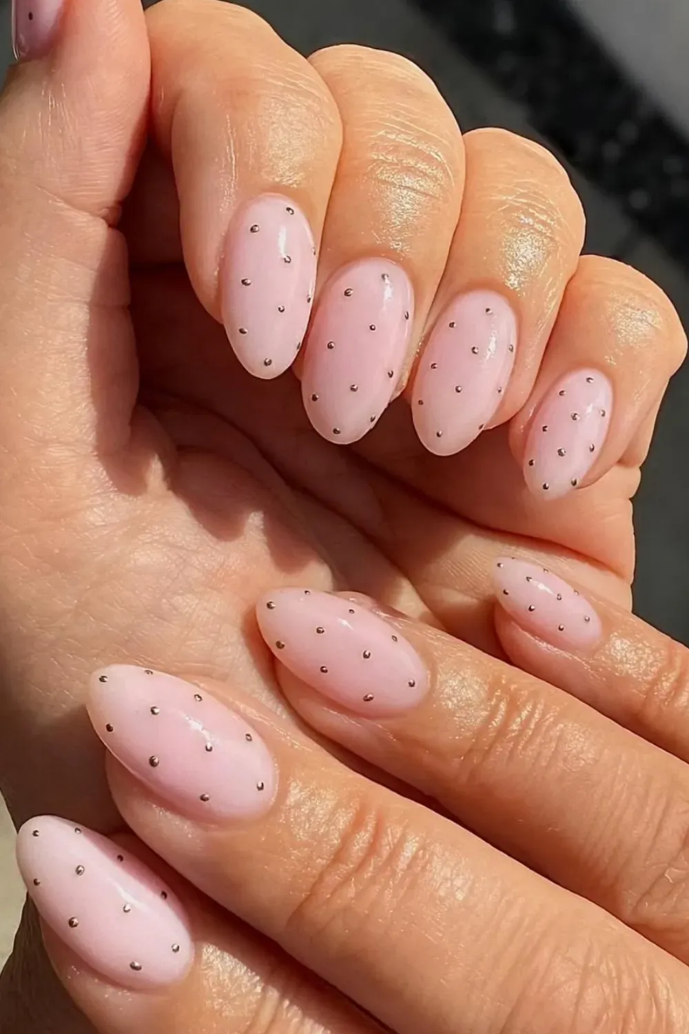 Oval-shaped nails with a pale pink sheer base, adorned with small, evenly spaced metallic gold studs or dots.