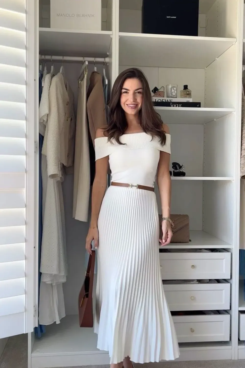 White Pleated Maxi Skirt and Off-Shoulder Top	Woman standing in a closet wearing a monochromatic white outfit: an off-the-shoulder knit top, a pleated maxi skirt, a thin brown belt, and white heels.