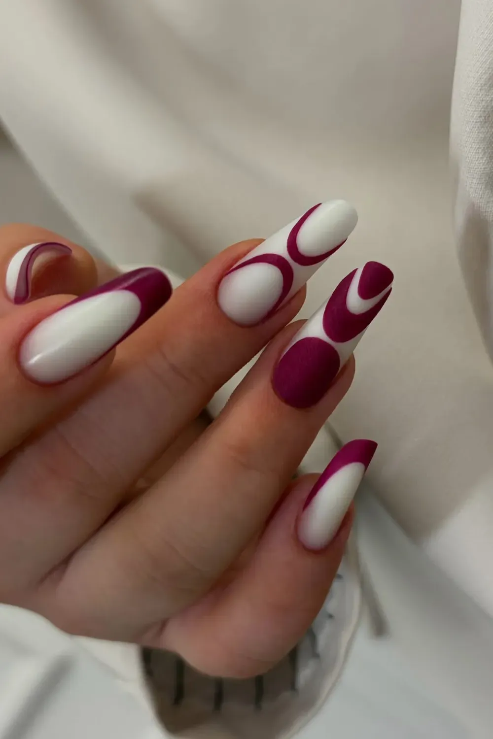 Abstract White and Magenta French Nails	Long coffin nails with a graphic, curved abstract French design in white and dark magenta.