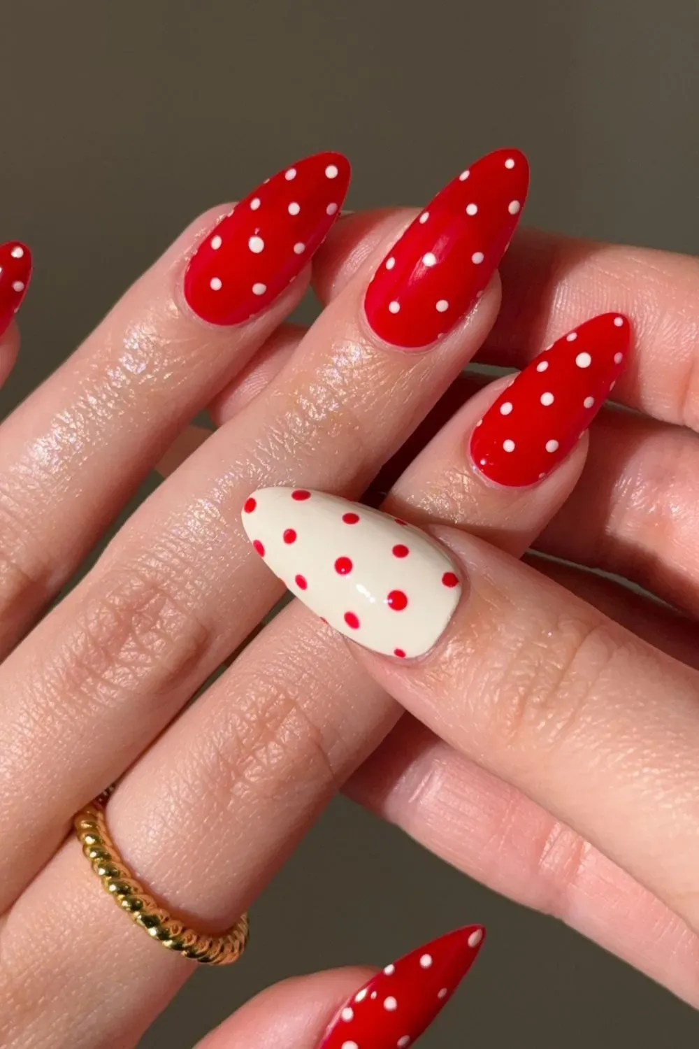Long almond nails with a bright red base and white polka dots, with one accent nail featuring a white base and red polka dots.