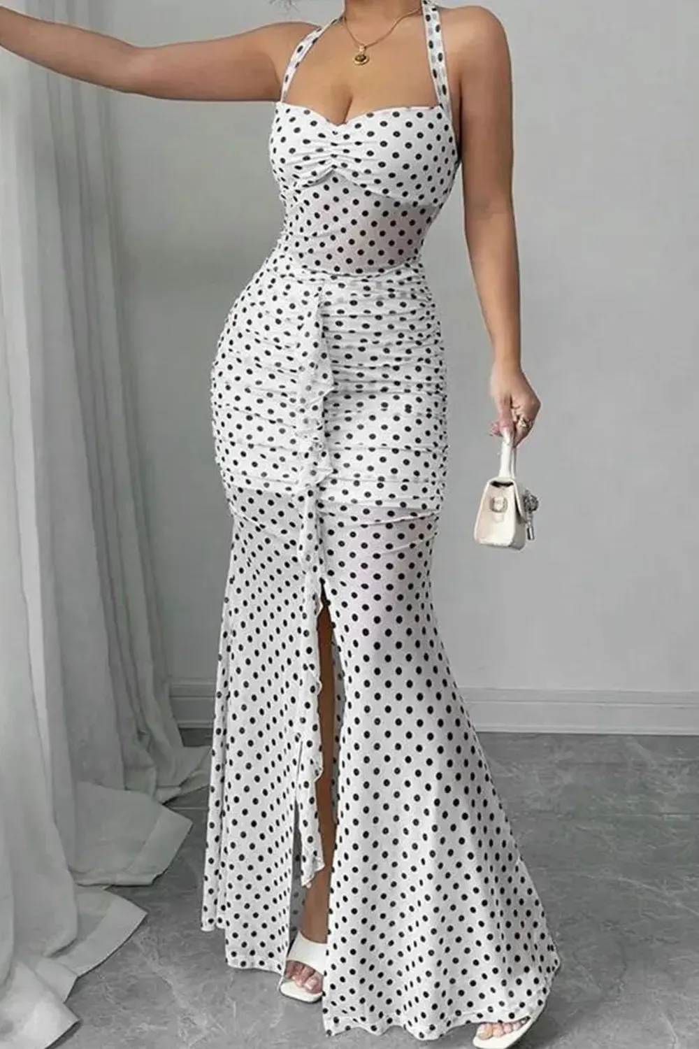 White Ruched Polka Dot Mermaid Gown	Woman in a fitted white mermaid gown with small black polka dots, a halter neck, and full-length ruching with a center slit.