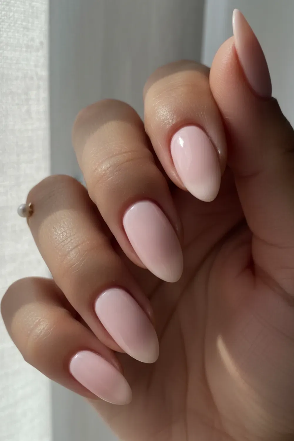 Simple Almond Pink Milky Manicure - Clean Girl Aesthetic - Hand featuring long, simple almond-shaped nails painted with a light, solid pink milky polish in natural sunlight.