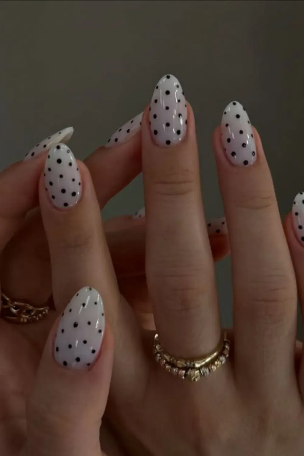 Almond-shaped nails with a sheer white base coat and evenly spaced small black polka dots.